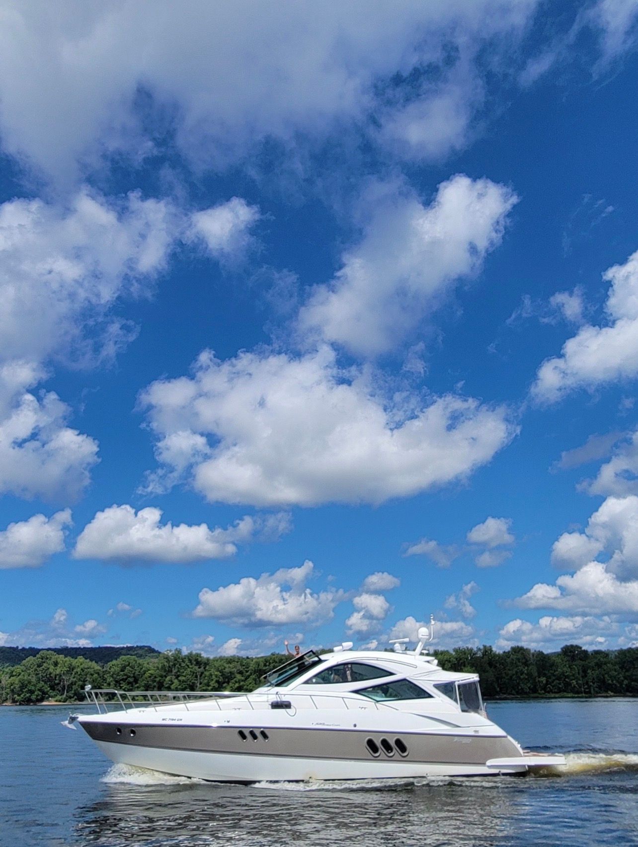 A white motor yacht cruises on calm water under a blue sky with clouds.