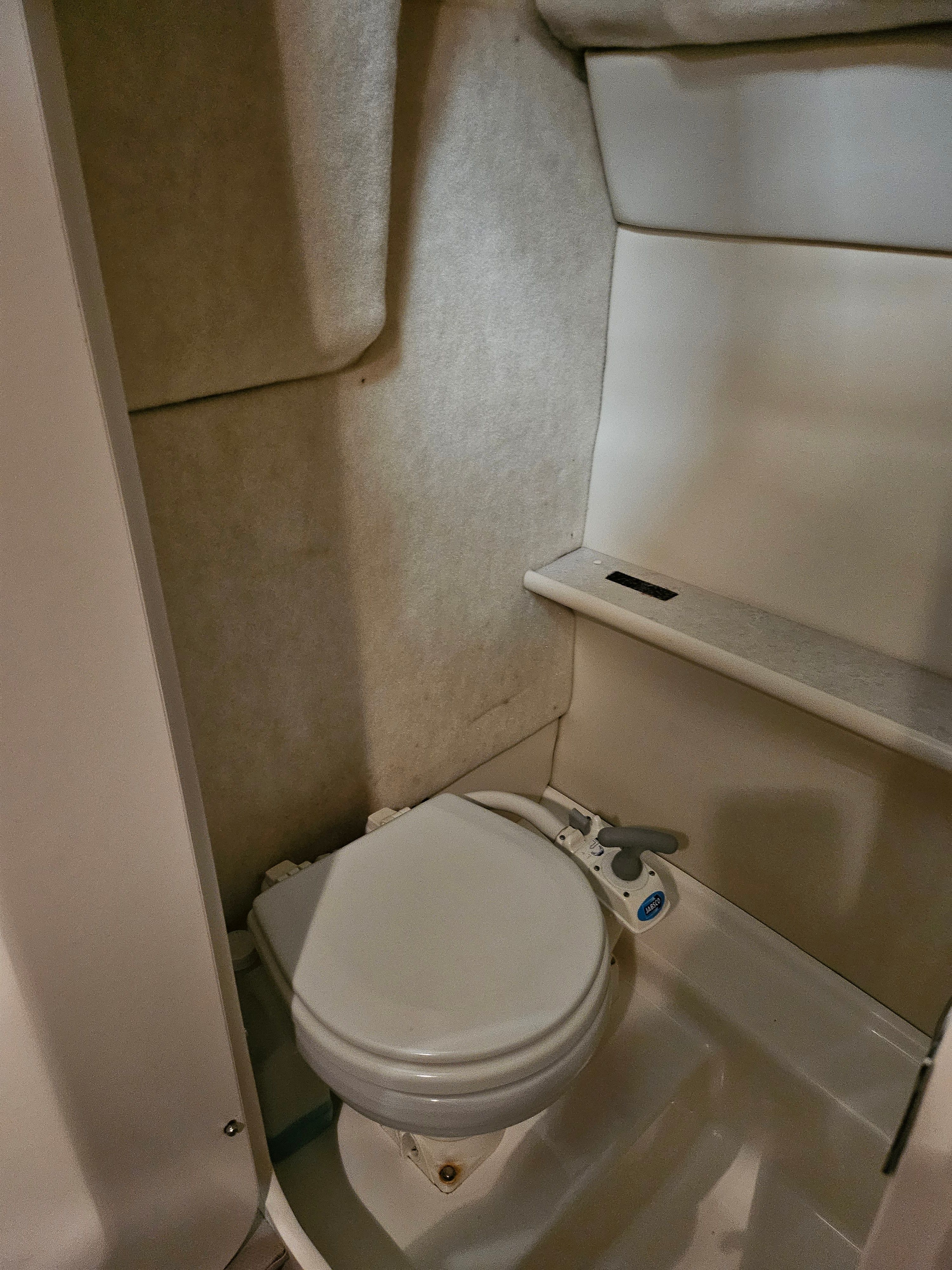 Interior view of a boat toilet with white walls and a small shelf.