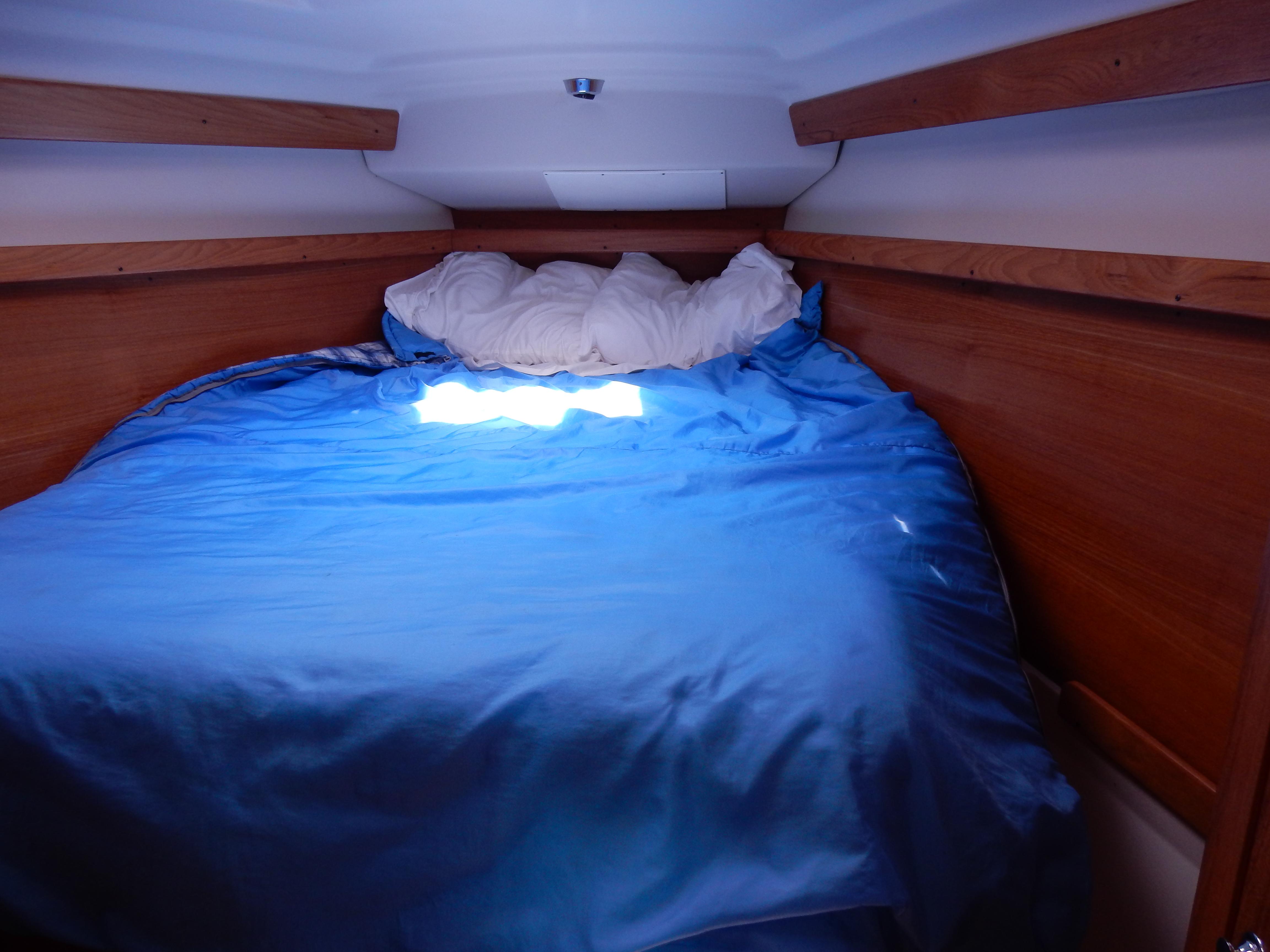 Cozy cabin bed with blue bedding in a 2004 Catalina 350 sailboat.