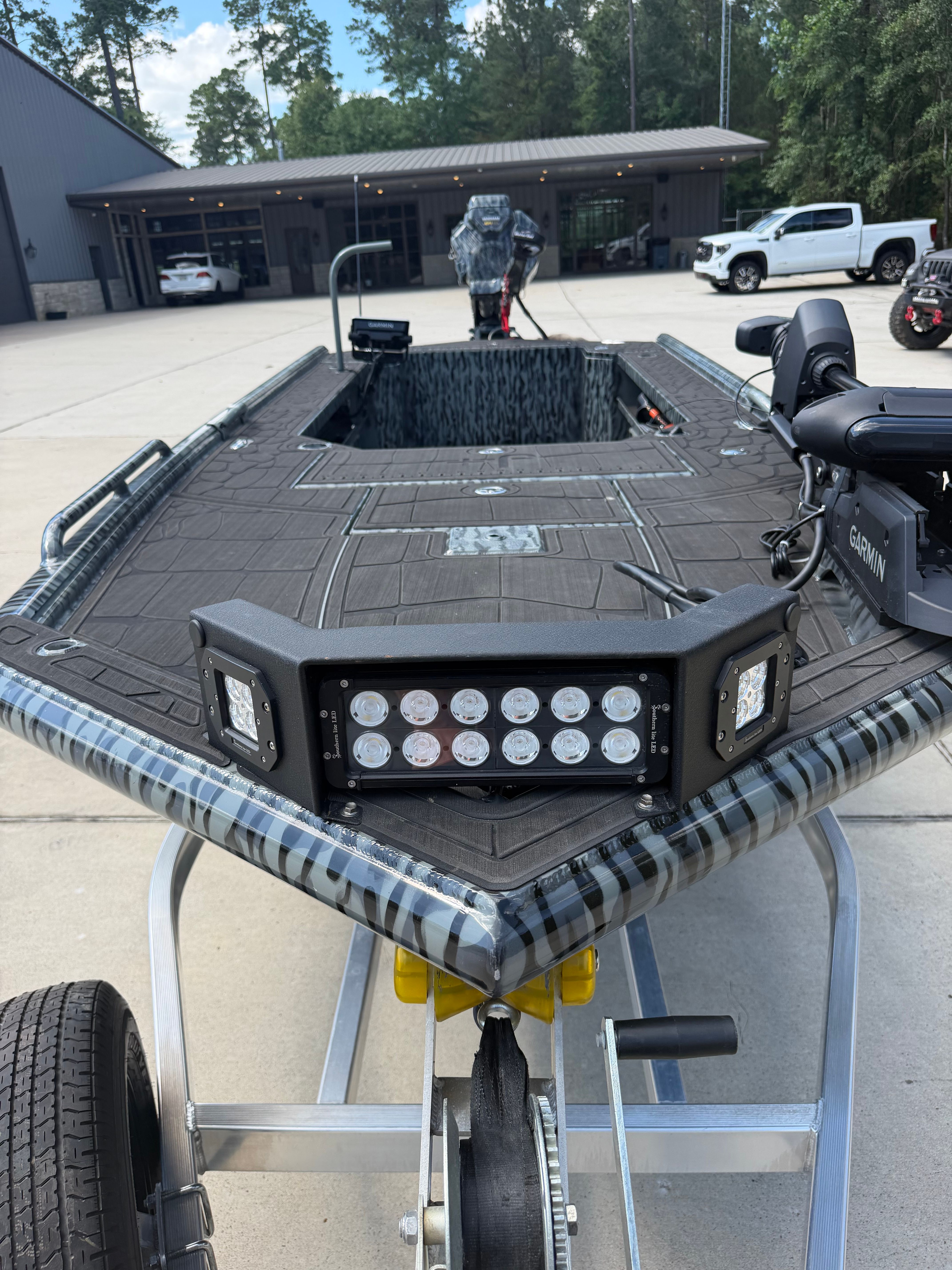 A modern boat on a trailer in front of a building, featuring LED lights and a motor.
