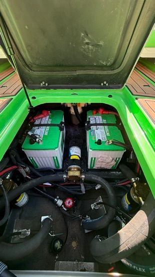 View of a green boat's engine compartment with two batteries and hoses.