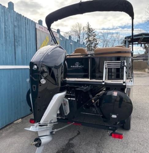 2025 Regency 230 LE3 pontoon boat with outboard motor, parked near blue fence.