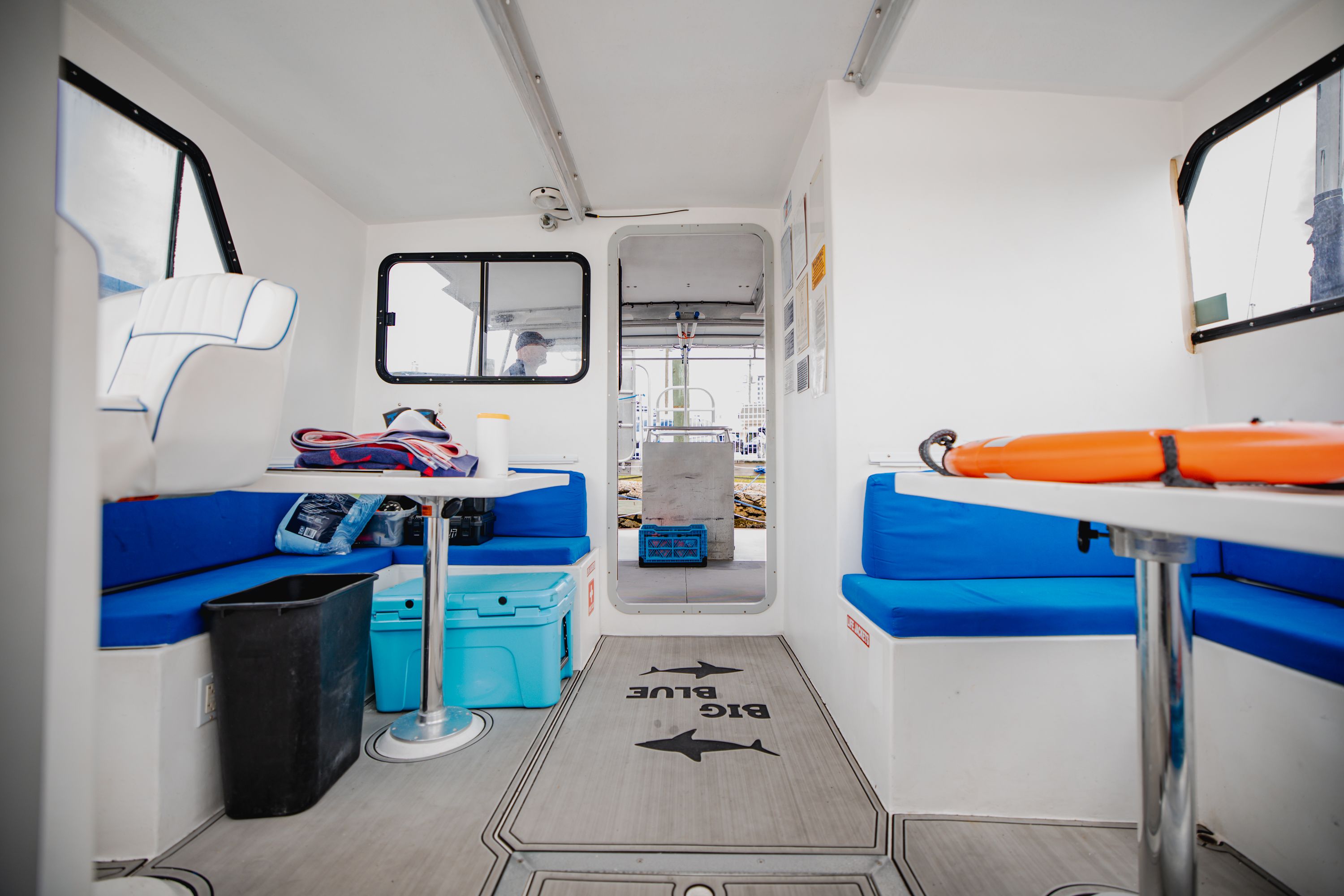 Interior of a dive boat with blue seating, tables, and a life ring.