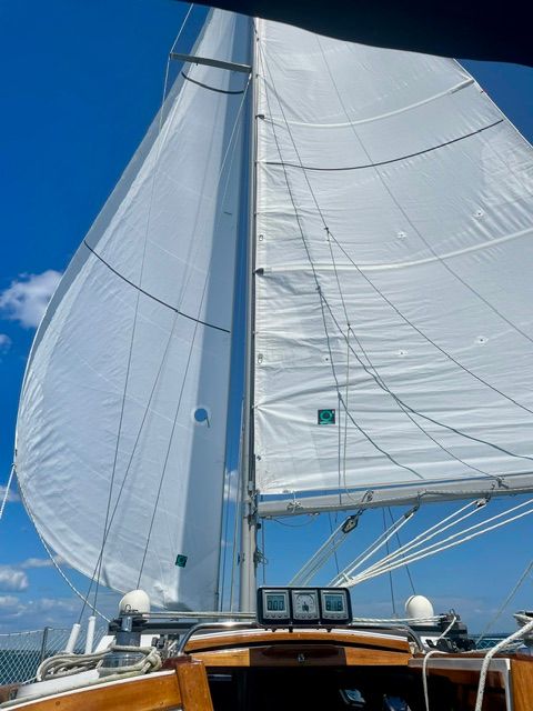 Sailboat with white sails under a blue sky, viewed from the cockpit.
