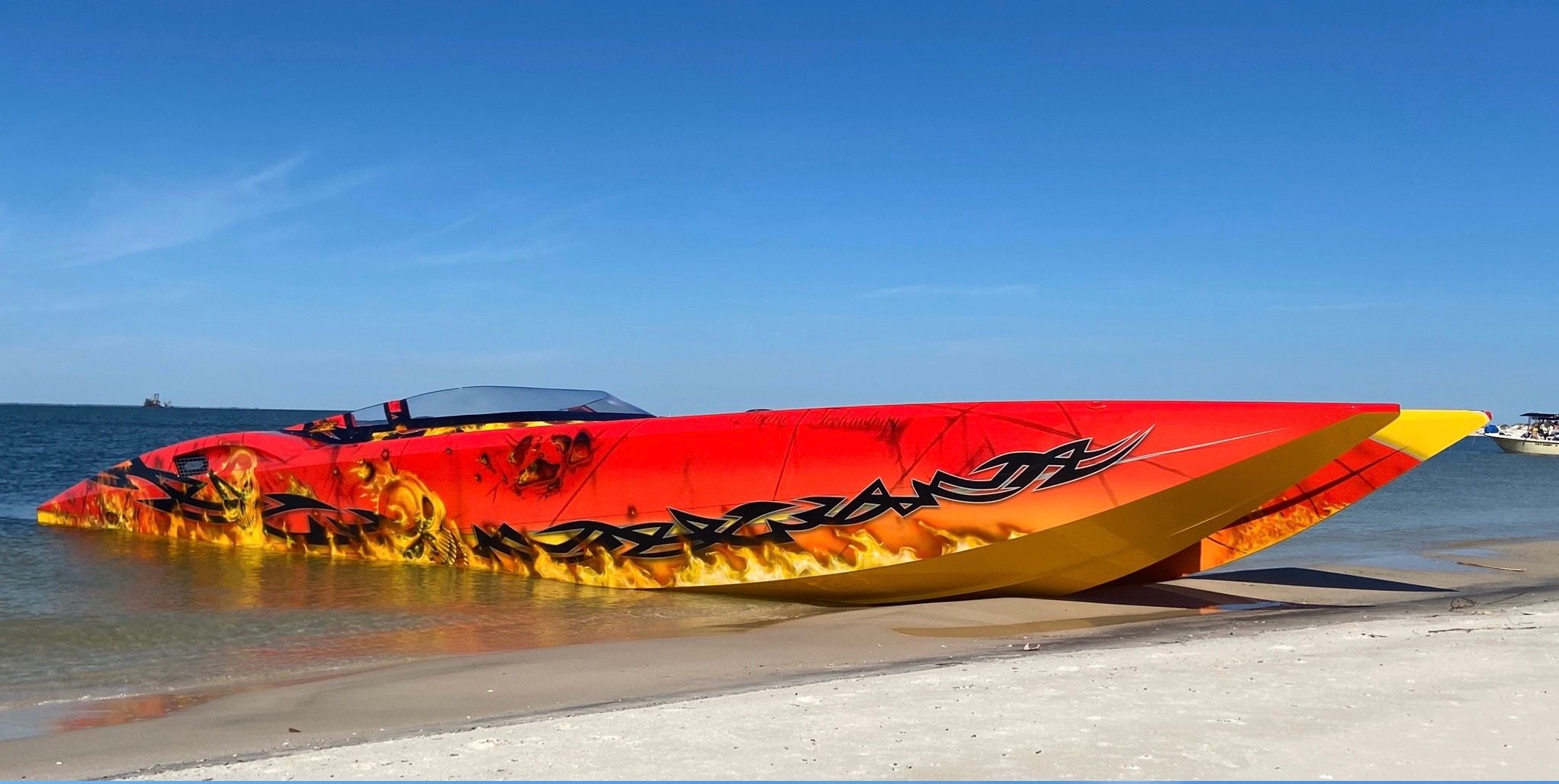 A vibrant red 2010 MTI CAT boat with flame graphics rests on the beach.
