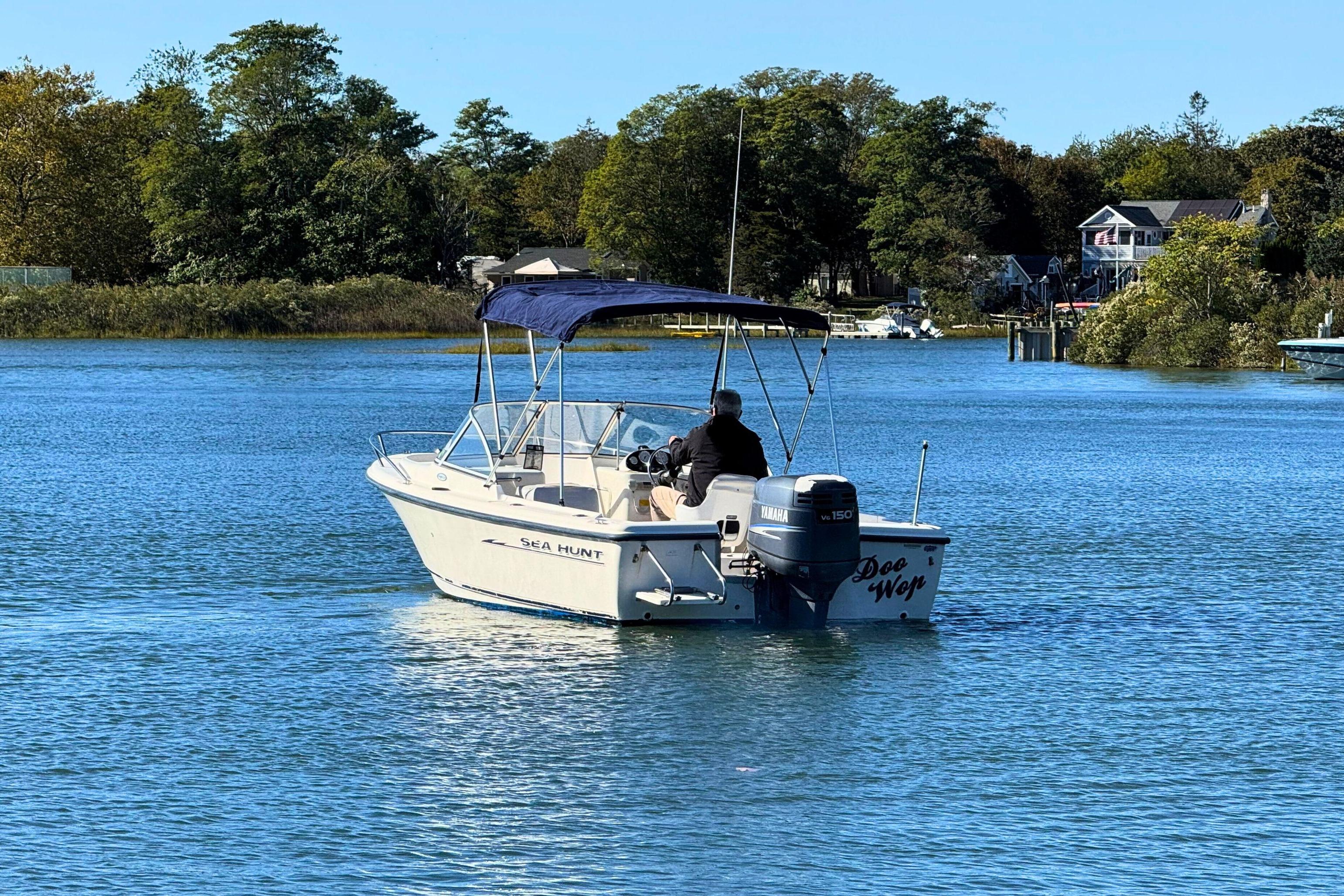 2002 Sea Hunt Escape 200 boat cruising on a serene lake with lush greenery.