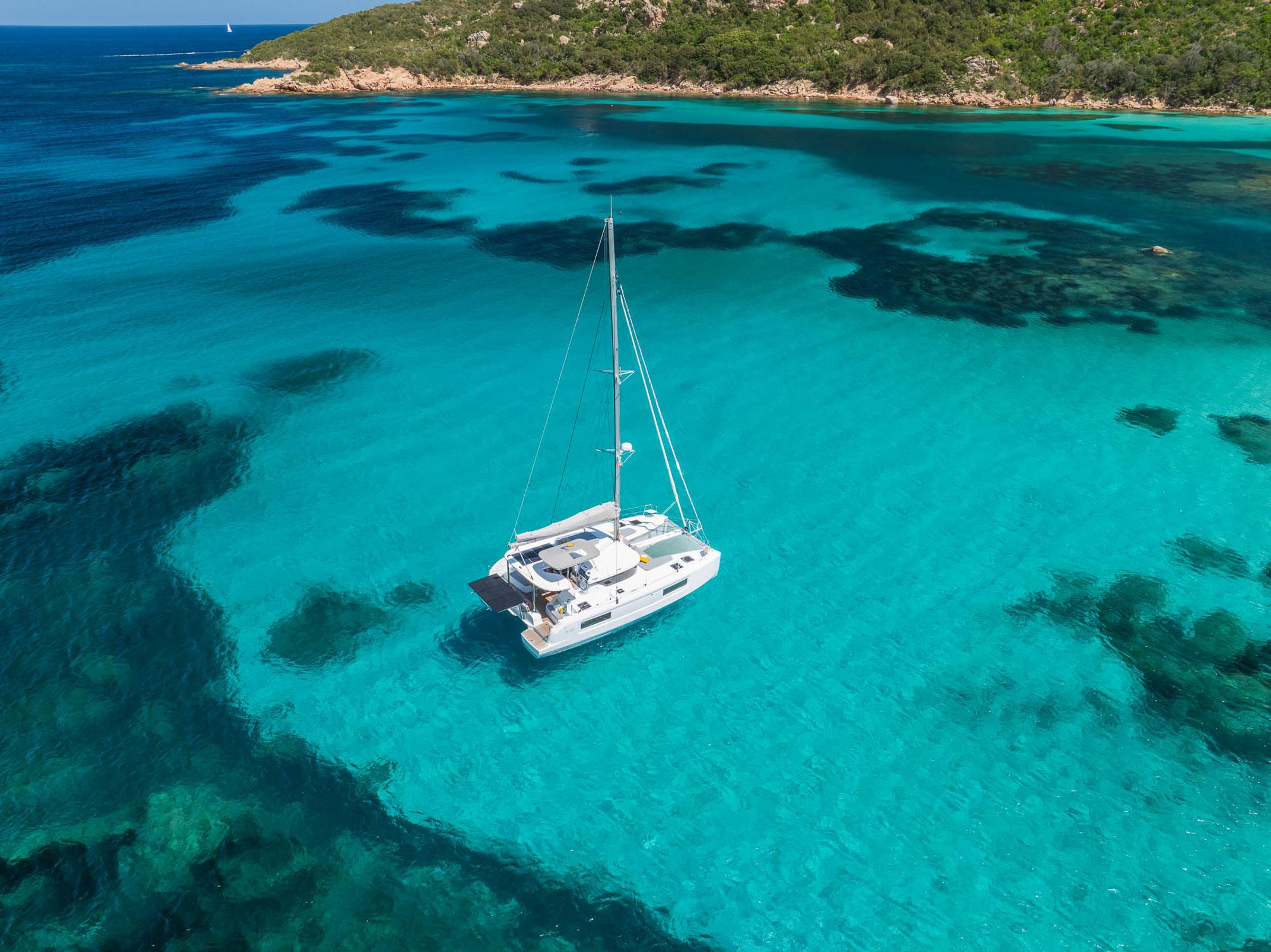 2025 Lagoon 38 catamaran sailing in clear turquoise waters near a lush coastline.