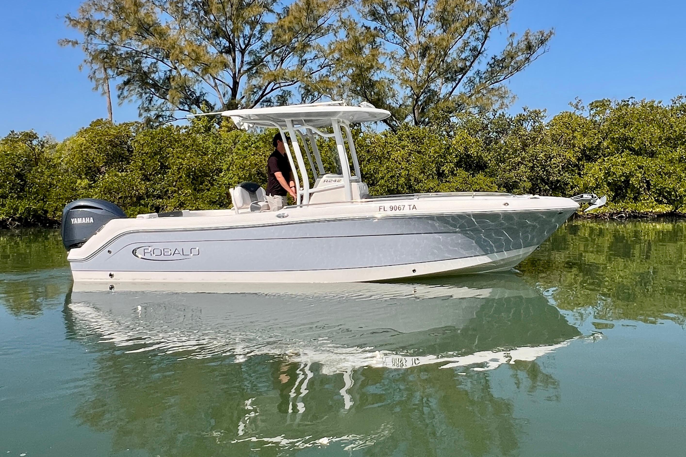 2021 Robalo R242 Explorer boat on calm water, surrounded by lush greenery.