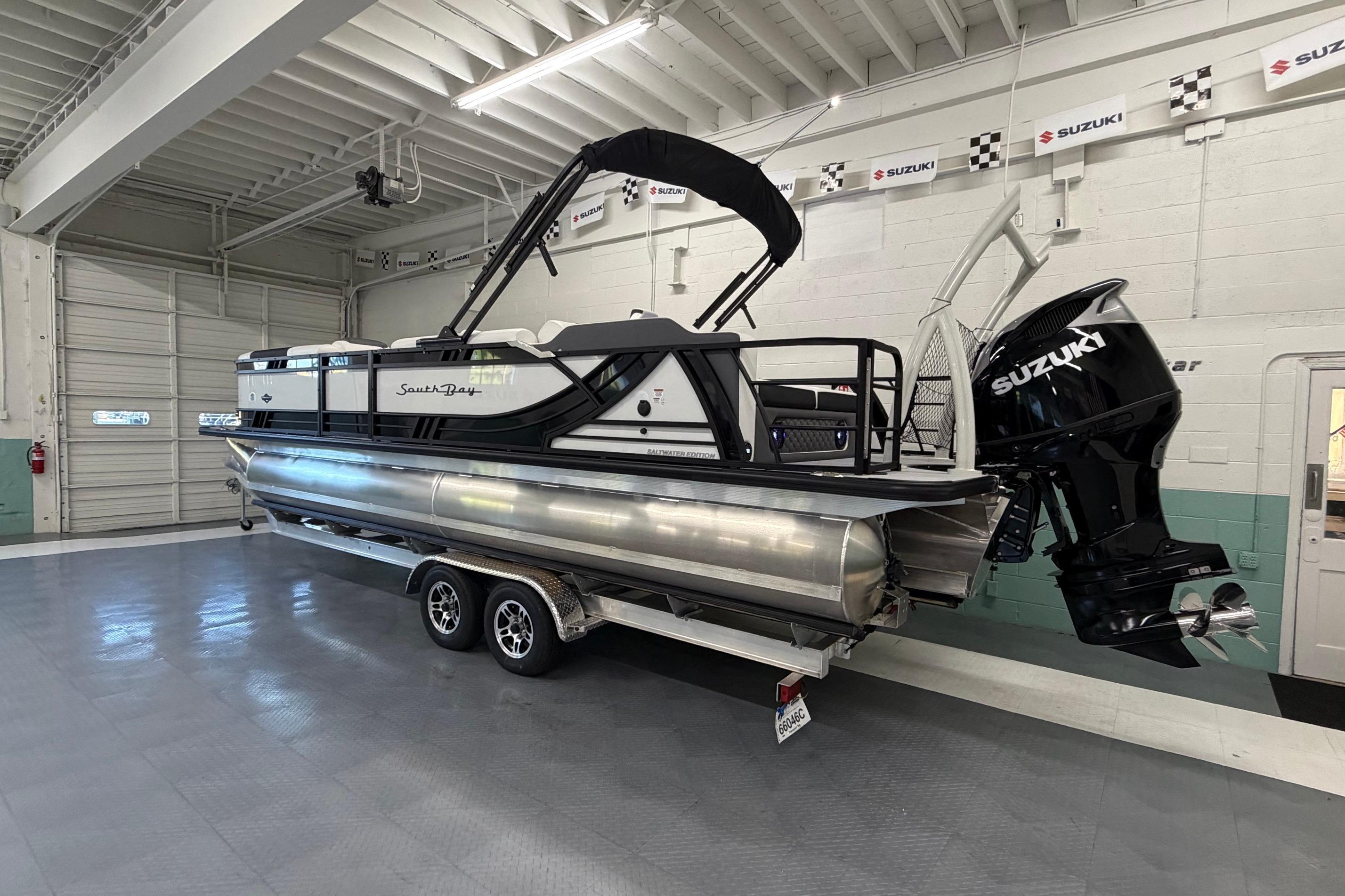 2026 South Bay 525SB2 pontoon boat with Suzuki engine in a showroom.