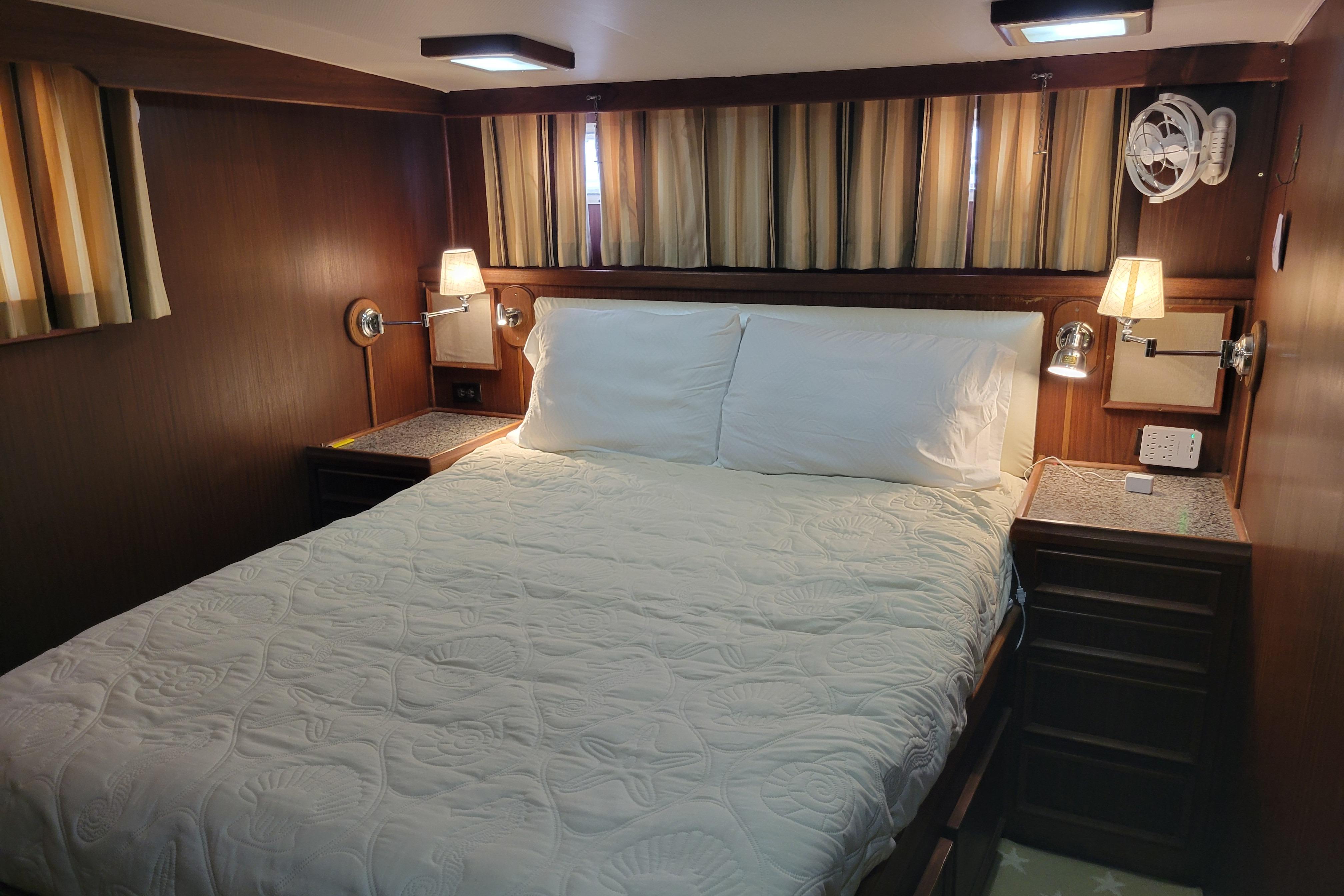 Cozy bedroom interior of 1980 Hatteras 53 Yacht Fisherman with wood paneling and soft lighting.