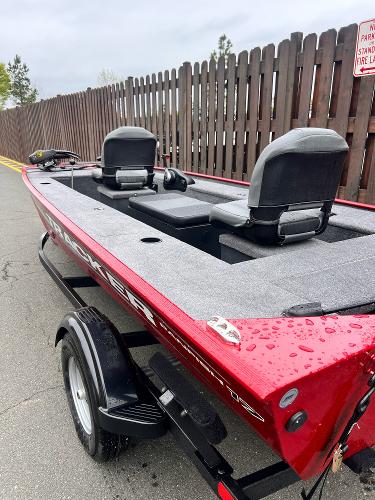 2025 Tracker Panfish 17 boat with red exterior, parked on a trailer near a wooden fence.