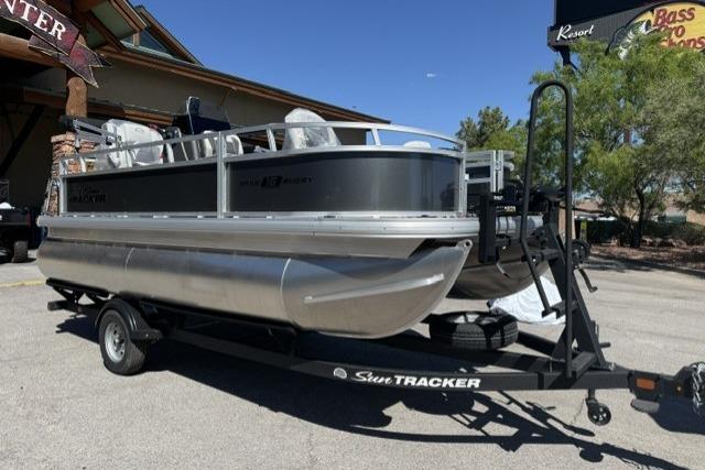 2026 Sun Tracker Bass Buggy 16 XL Select pontoon boat on trailer in outdoor setting.