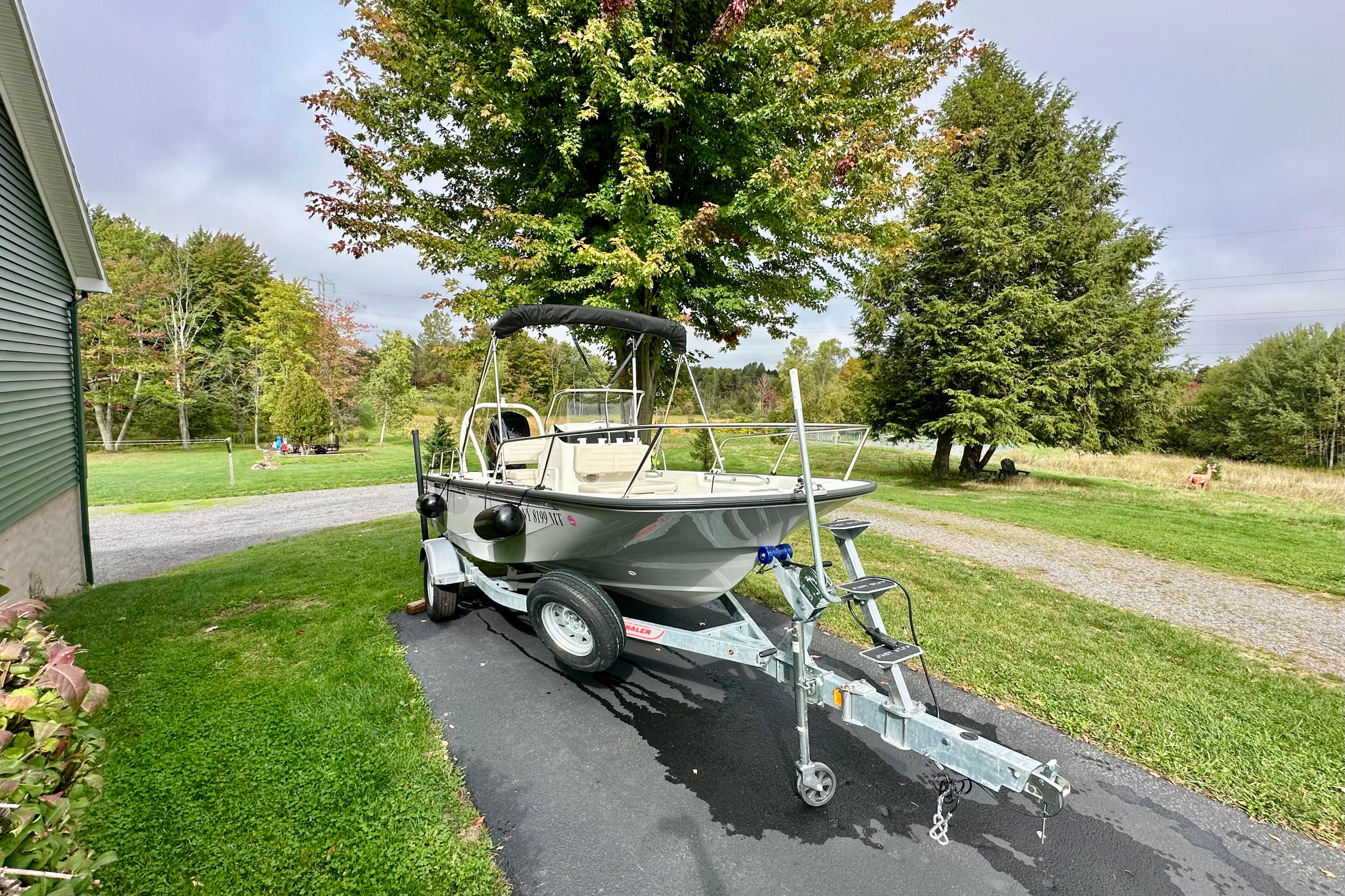 2024 Boston Whaler 170 Montauk boat on trailer, parked on driveway near lush greenery.