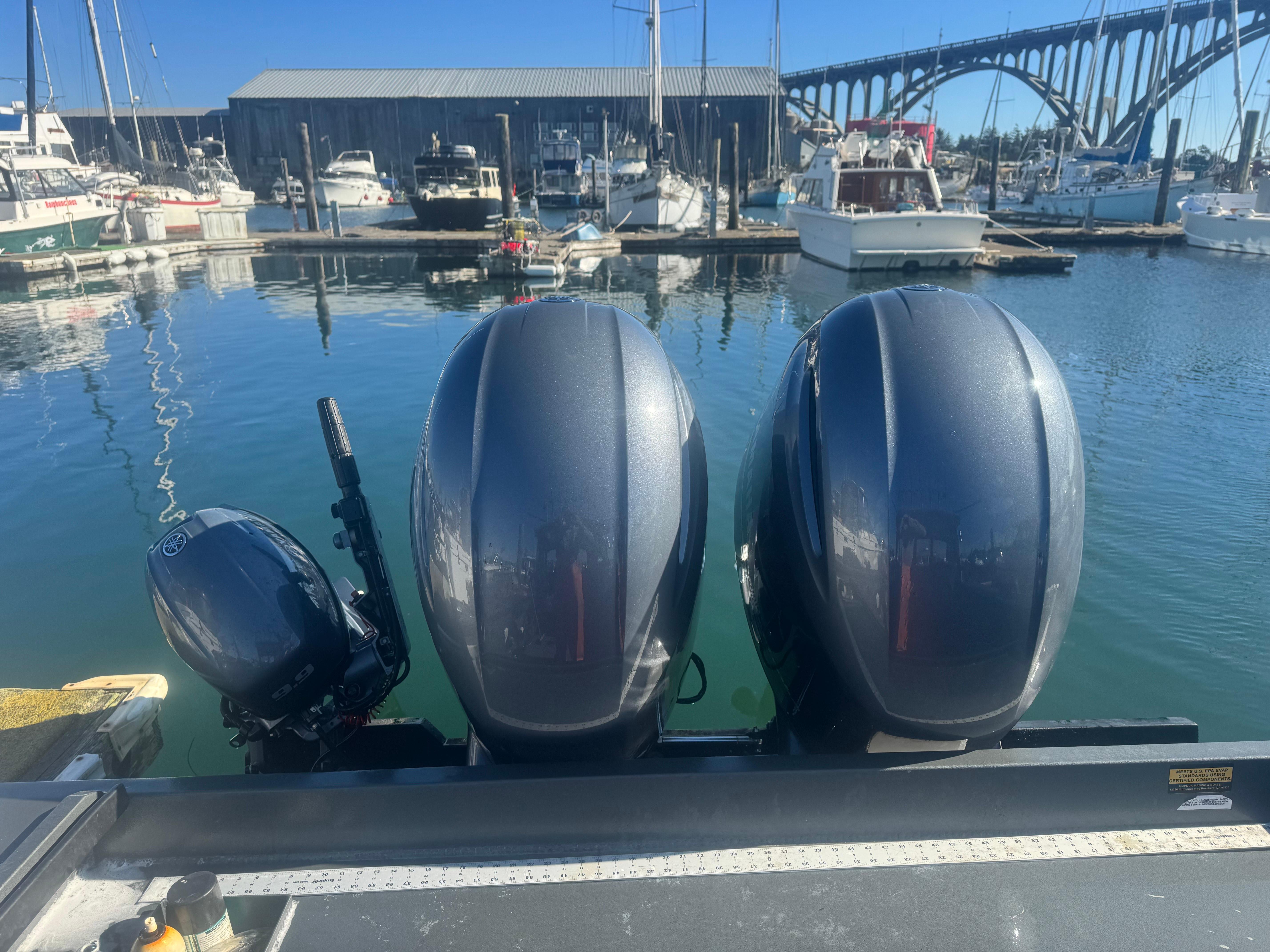 Three outboard motors on a 2022 Custom Umpqua Marina 26 bay series boat at a marina.