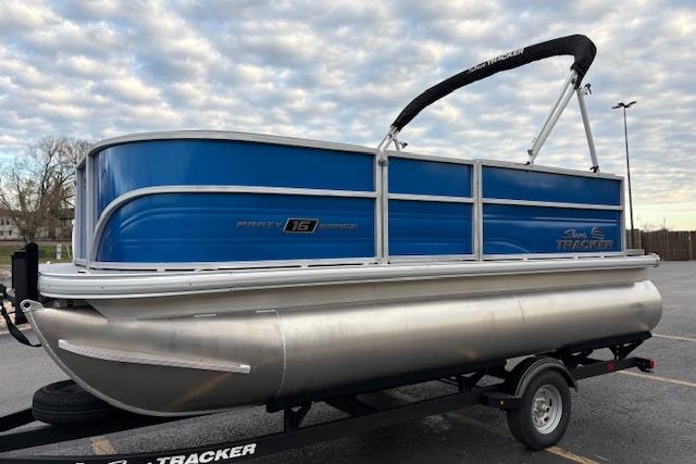 2026 Sun Tracker Party Barge 16 DLX pontoon boat on trailer, blue and silver design.