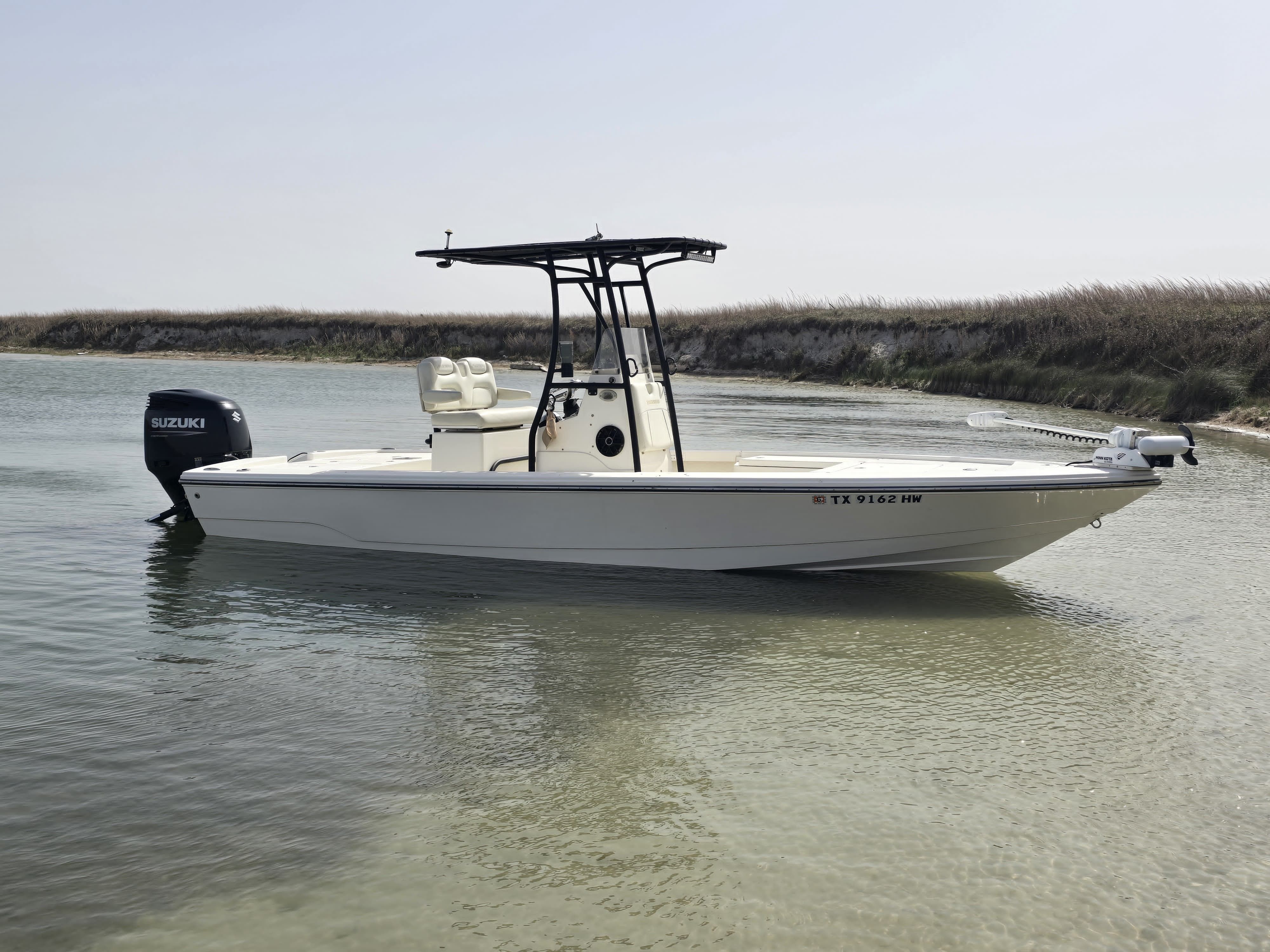 A white boat with a black canopy on shallow water near a sandy shoreline.