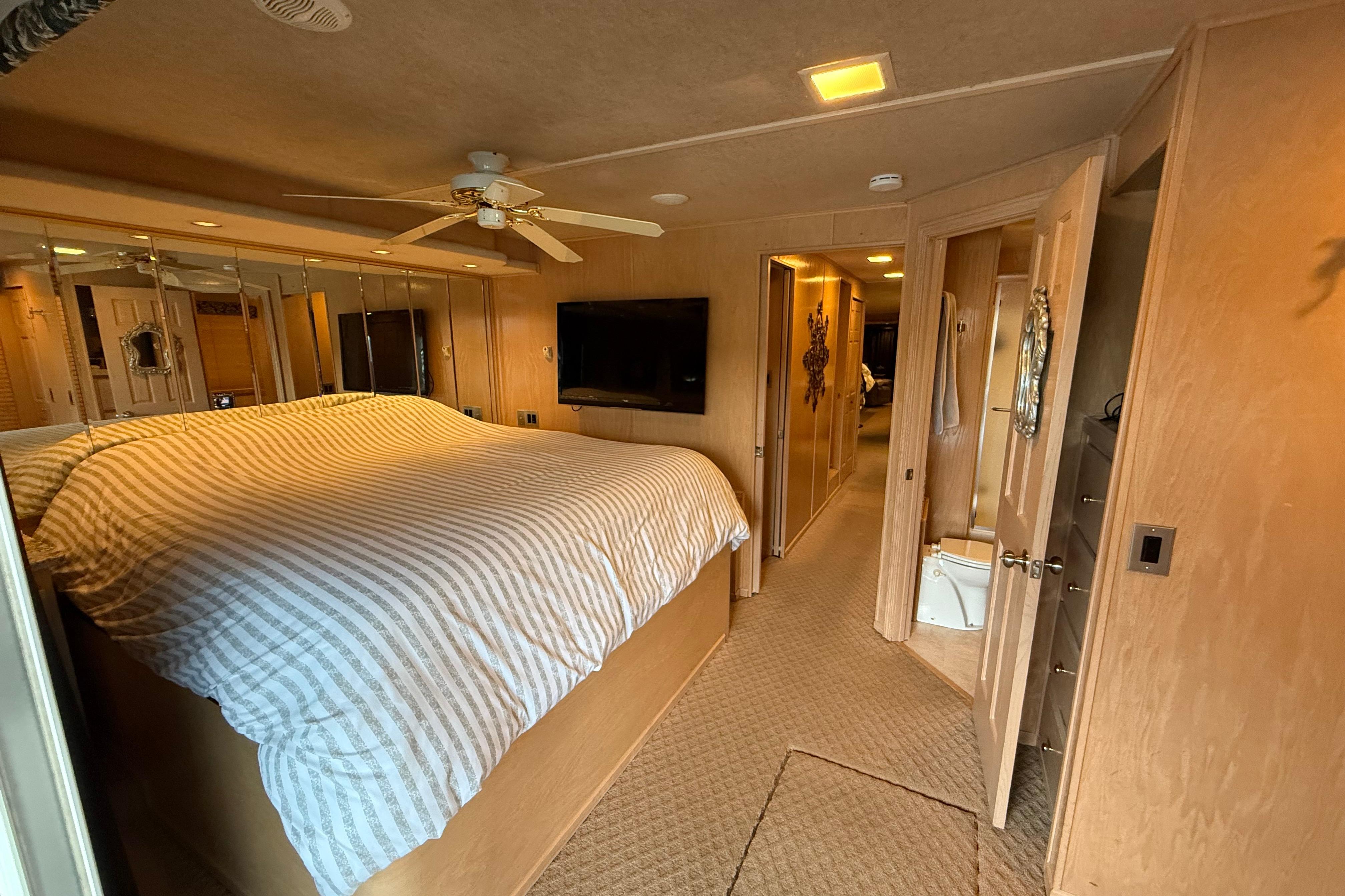 Bedroom interior of 1998 Sumerset 16x76 houseboat with striped bedding and ceiling fan.