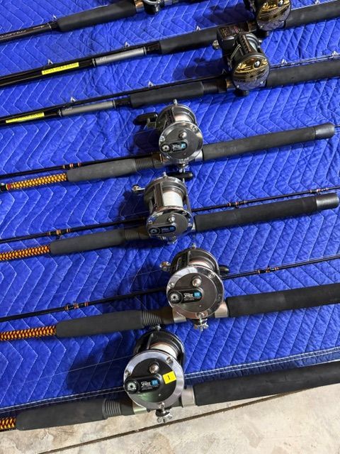 Several fishing rods with reels are laid out on a blue padded blanket.