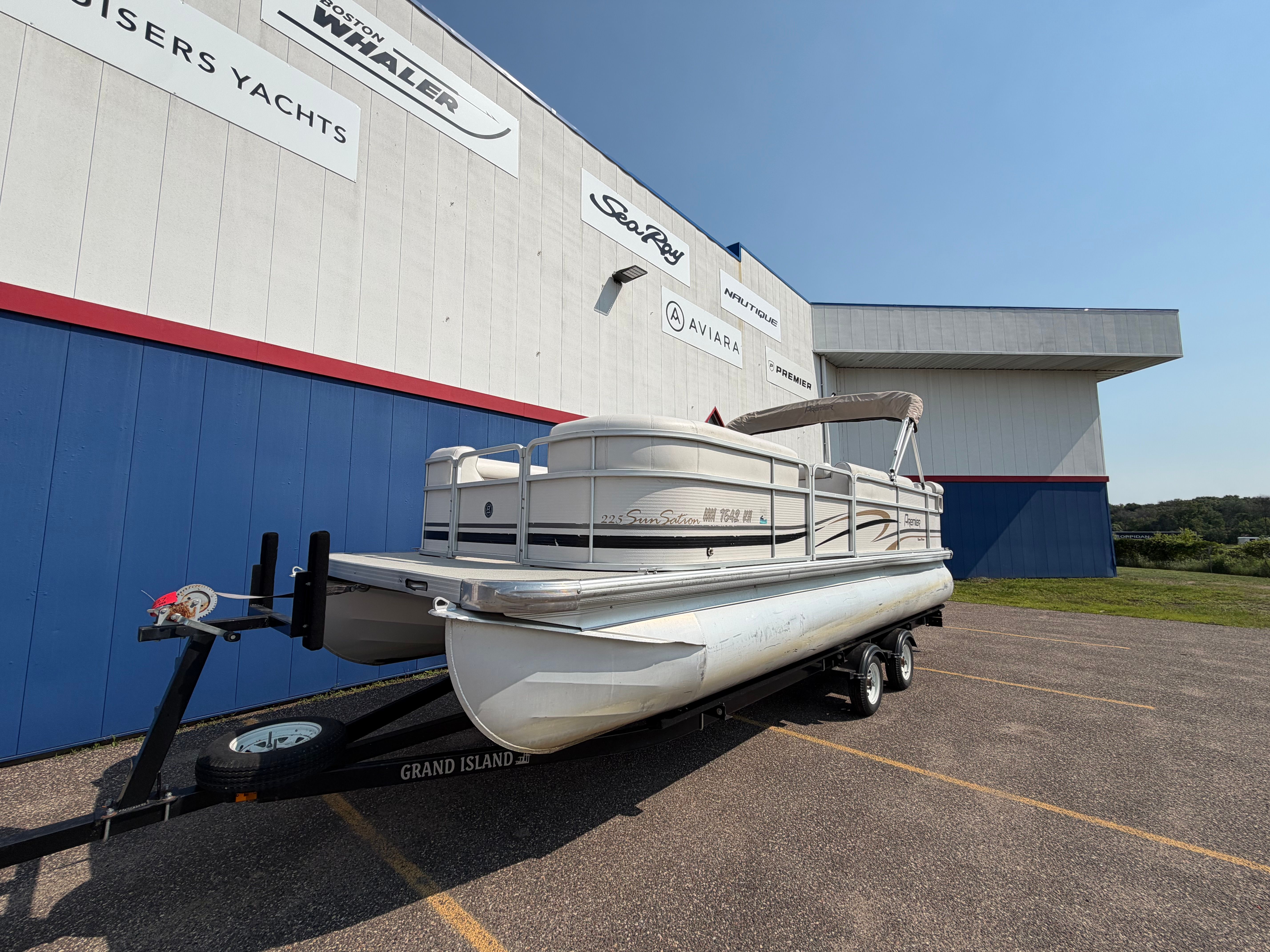 A 2007 Premier 225 Sunsation pontoon boat on a trailer in front of a building.