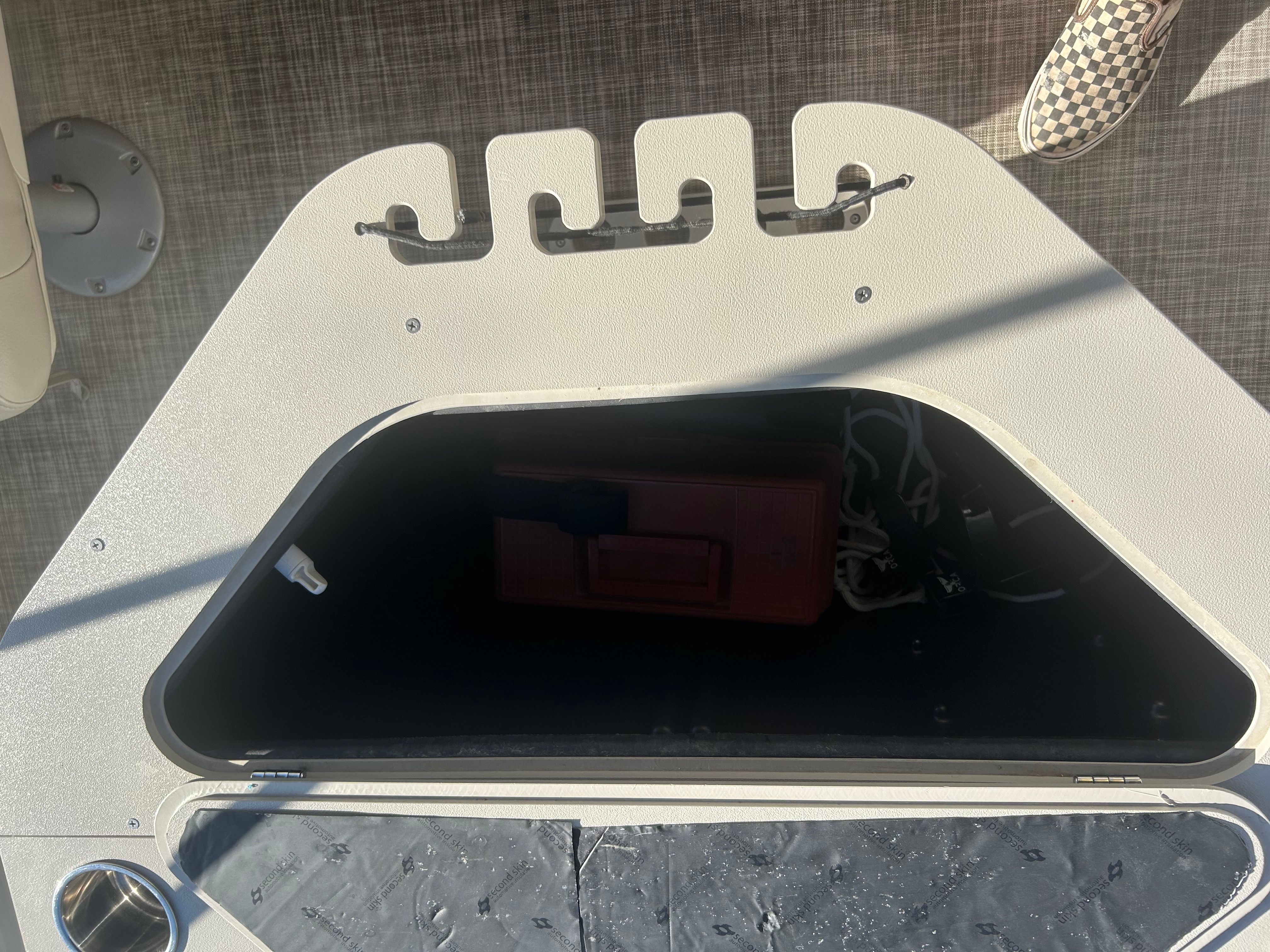 An open storage compartment on a boat with a red container and ropes inside.