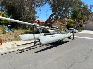 A Prindle 19 catamaran is on a trailer in a residential street.