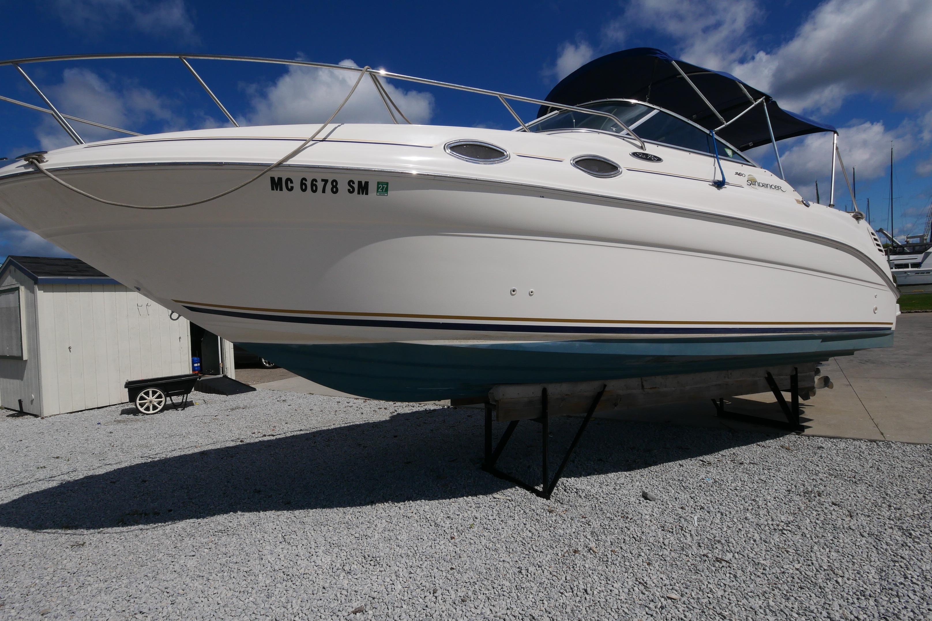 2003 Sea Ray 260 Sundancer boat on display, white hull, blue canopy, sunny day.