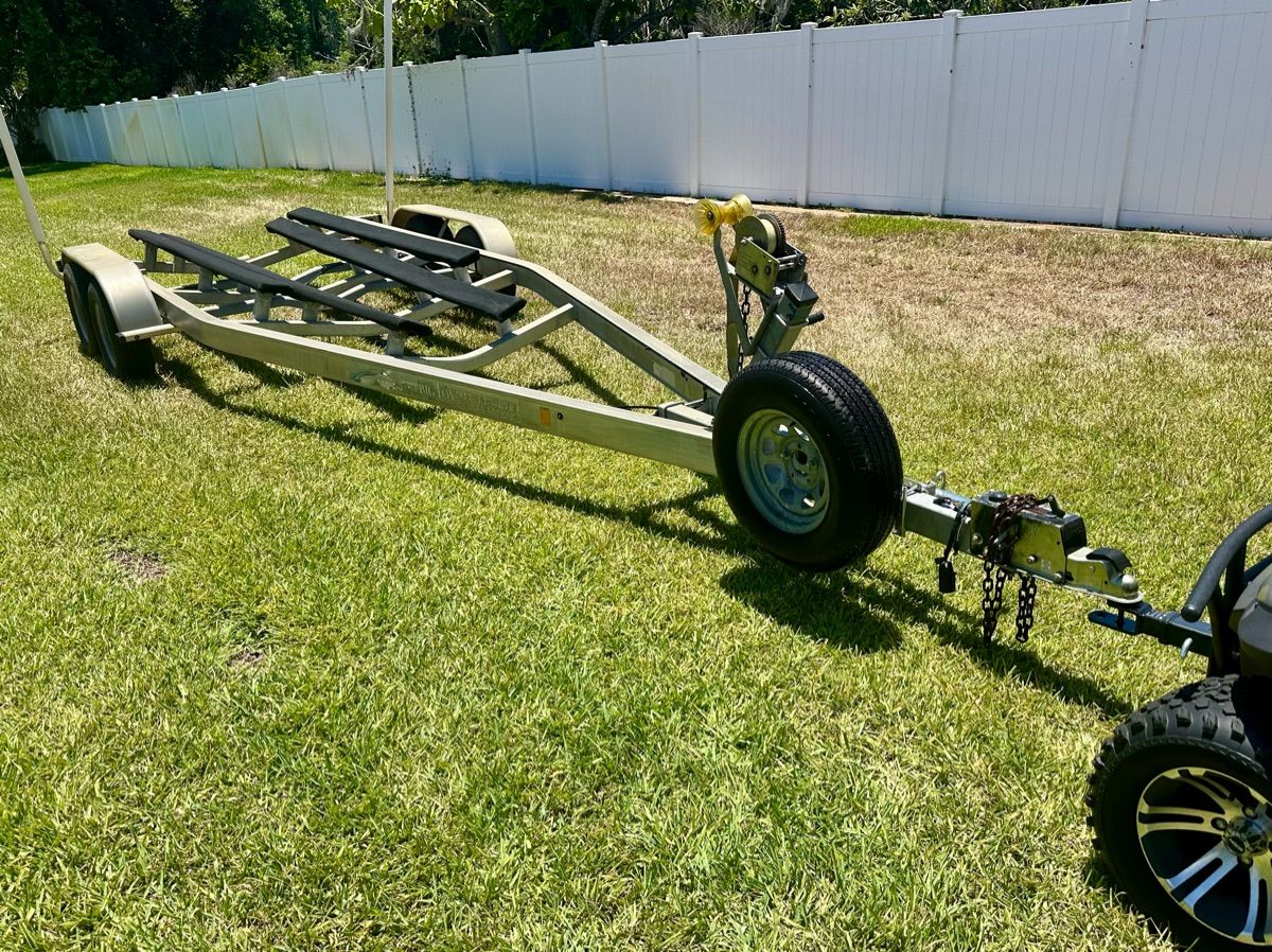 Boat trailer on grass with a white fence in the background.