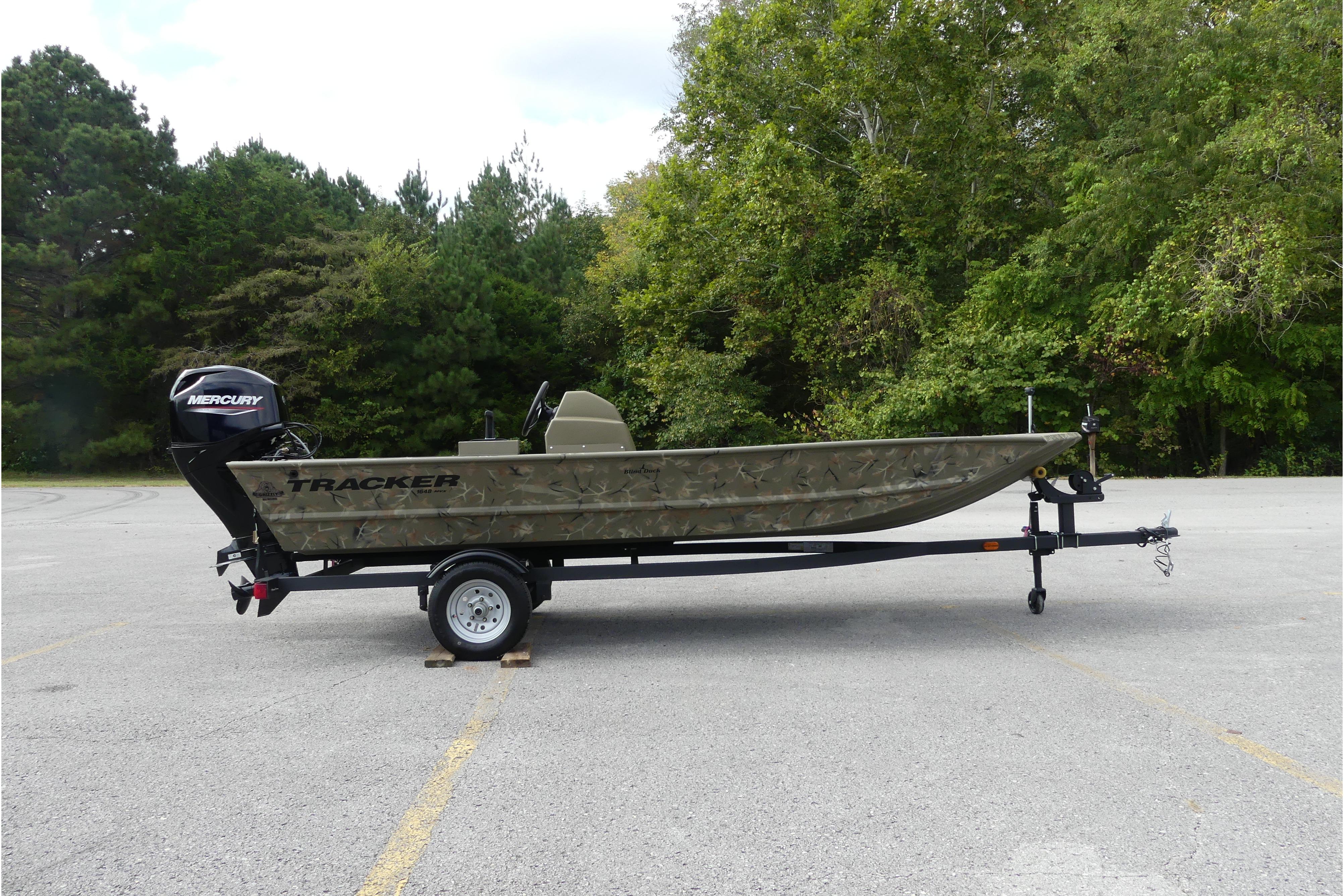 2025 Tracker Grizzly 1648 SC boat on trailer in a wooded parking area.