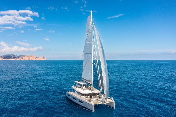 2025 Lagoon 60 catamaran sailing on open sea under clear blue sky.