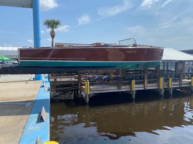 Grand Craft Classic Runabout 2000 on dock, wooden design, sunny day, palm tree nearby.