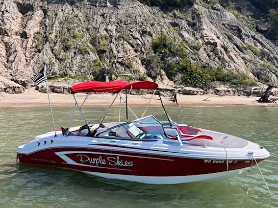 A red Chaparral boat with a sunshade floats in clear water near a rocky shoreline.