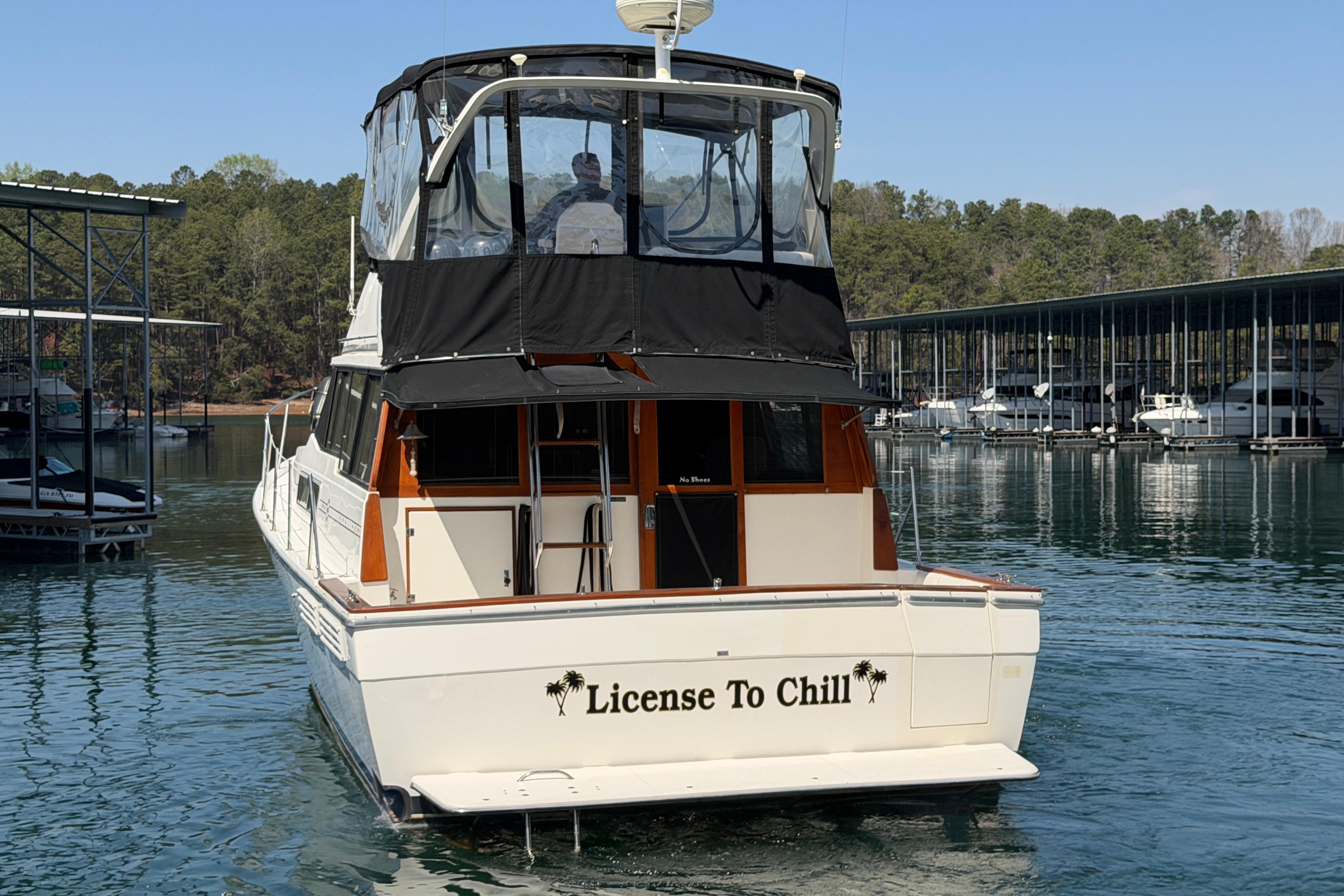 1994 Bayliner 3888 MY Sedan boat named "License To Chill" docked on a serene lake.