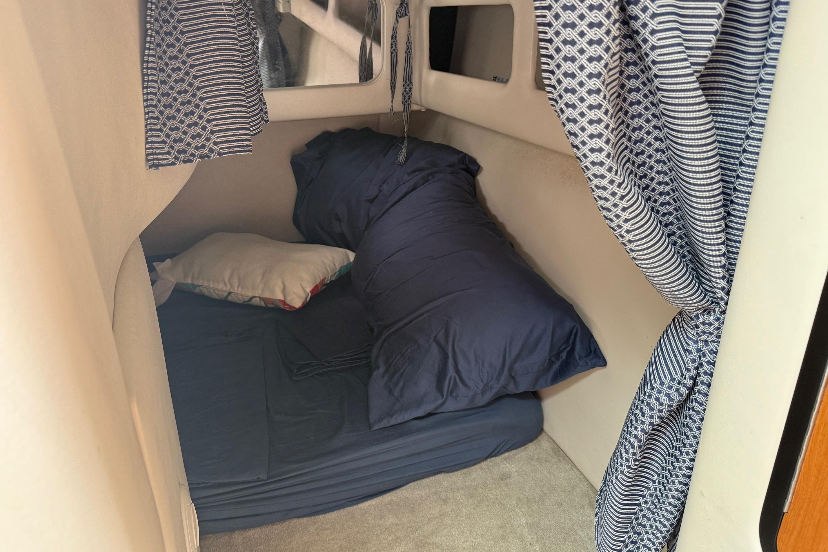 Cozy cabin interior of 2005 Crownline 250 CR boat with blue bedding and patterned curtains.