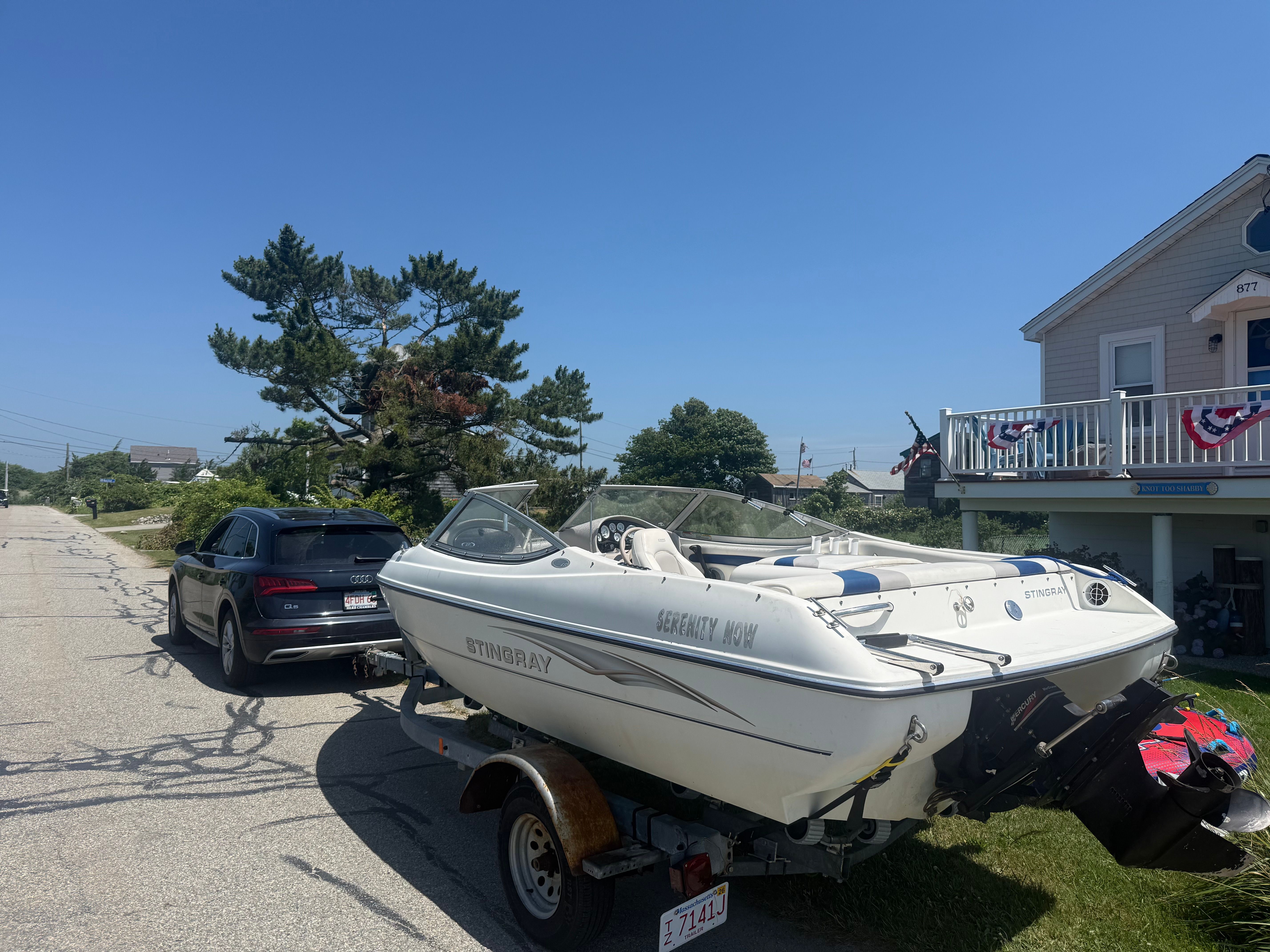 A white 2003 Stingray boat on a trailer, parked next to a car on a street.