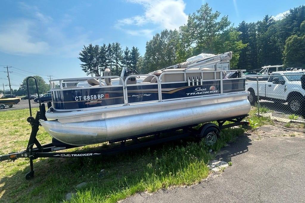 2023 Sun Tracker Bass Buggy 18 DLX pontoon boat on trailer, parked outdoors.