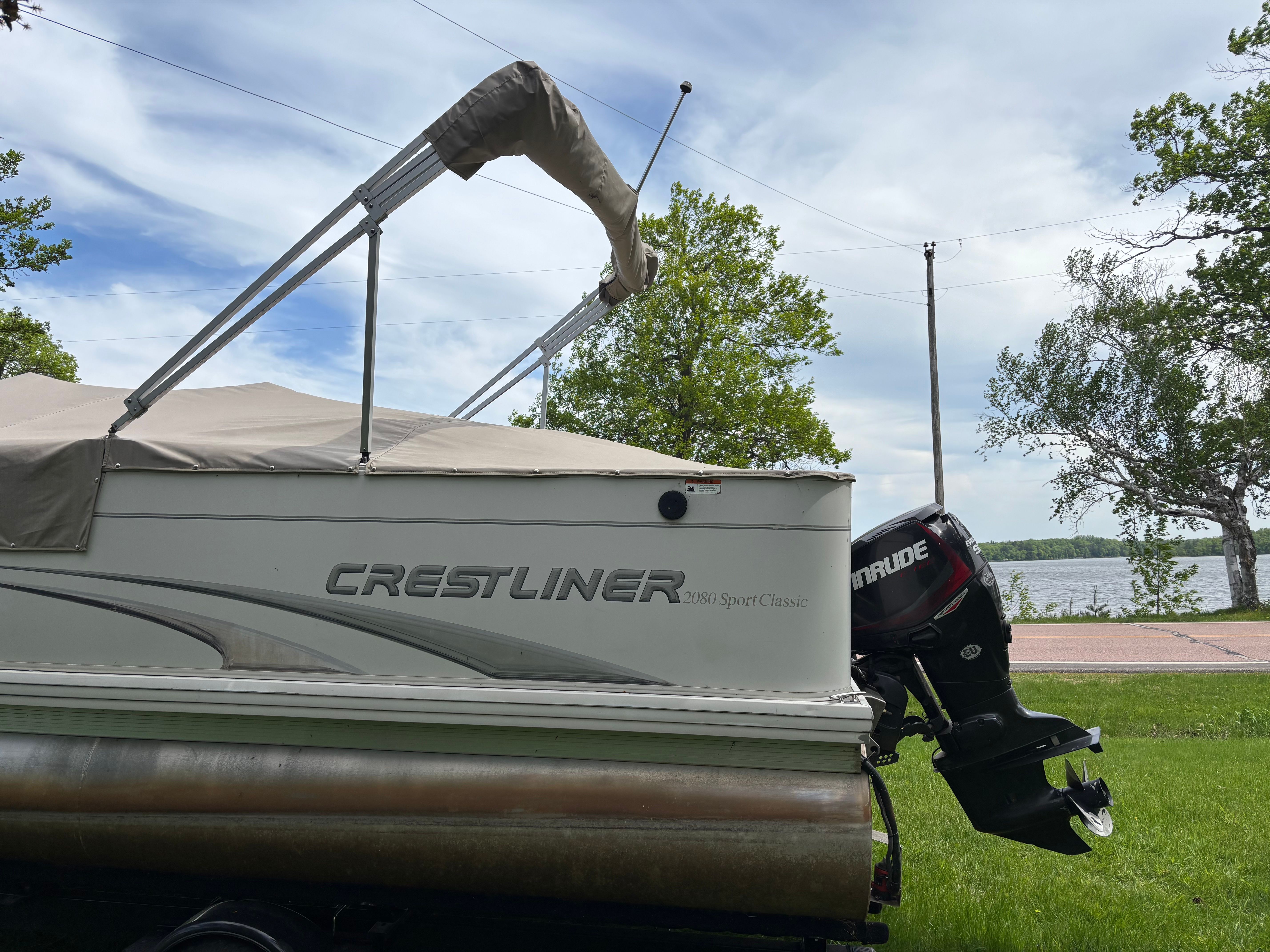 A 2004 Crestliner 2080 SPORT boat with an outboard motor, parked on a trailer on land.