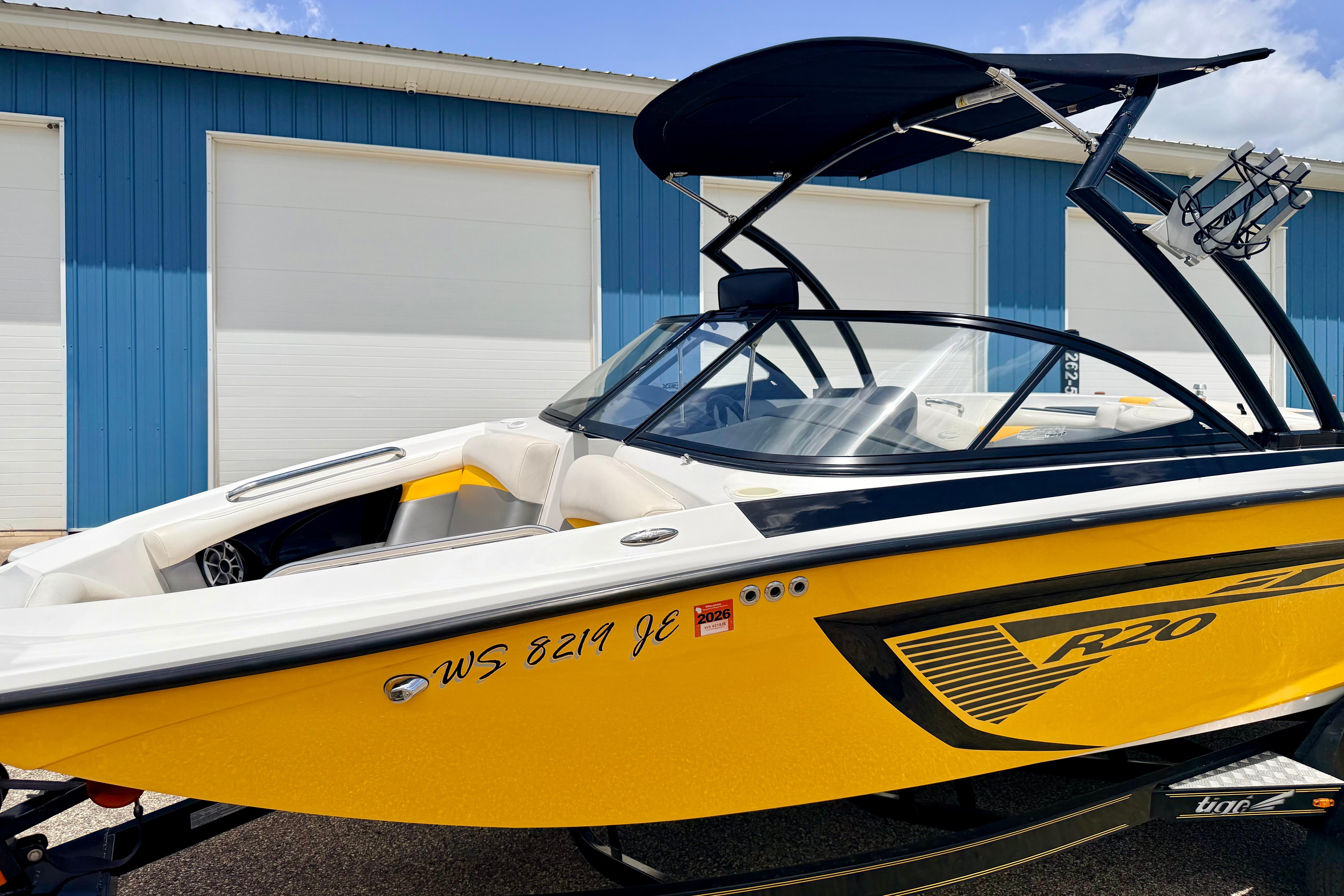 2014 Tigé R20 boat with yellow hull, parked near blue building.