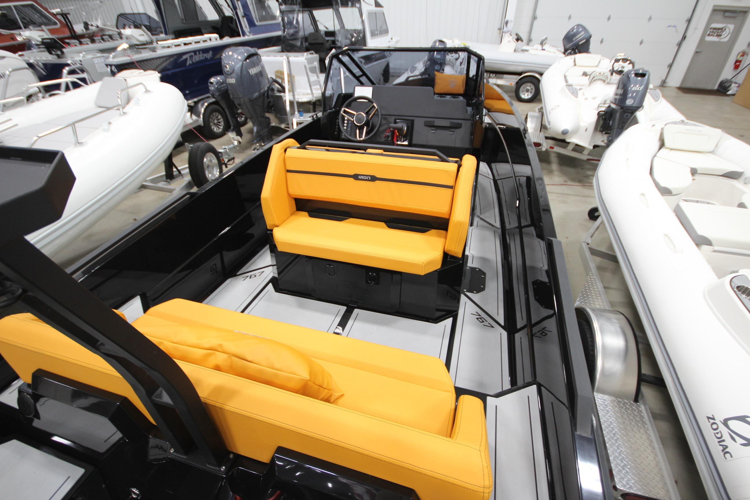 2026 Iron 767 boat with vibrant orange seating, showcased in a showroom among other boats.