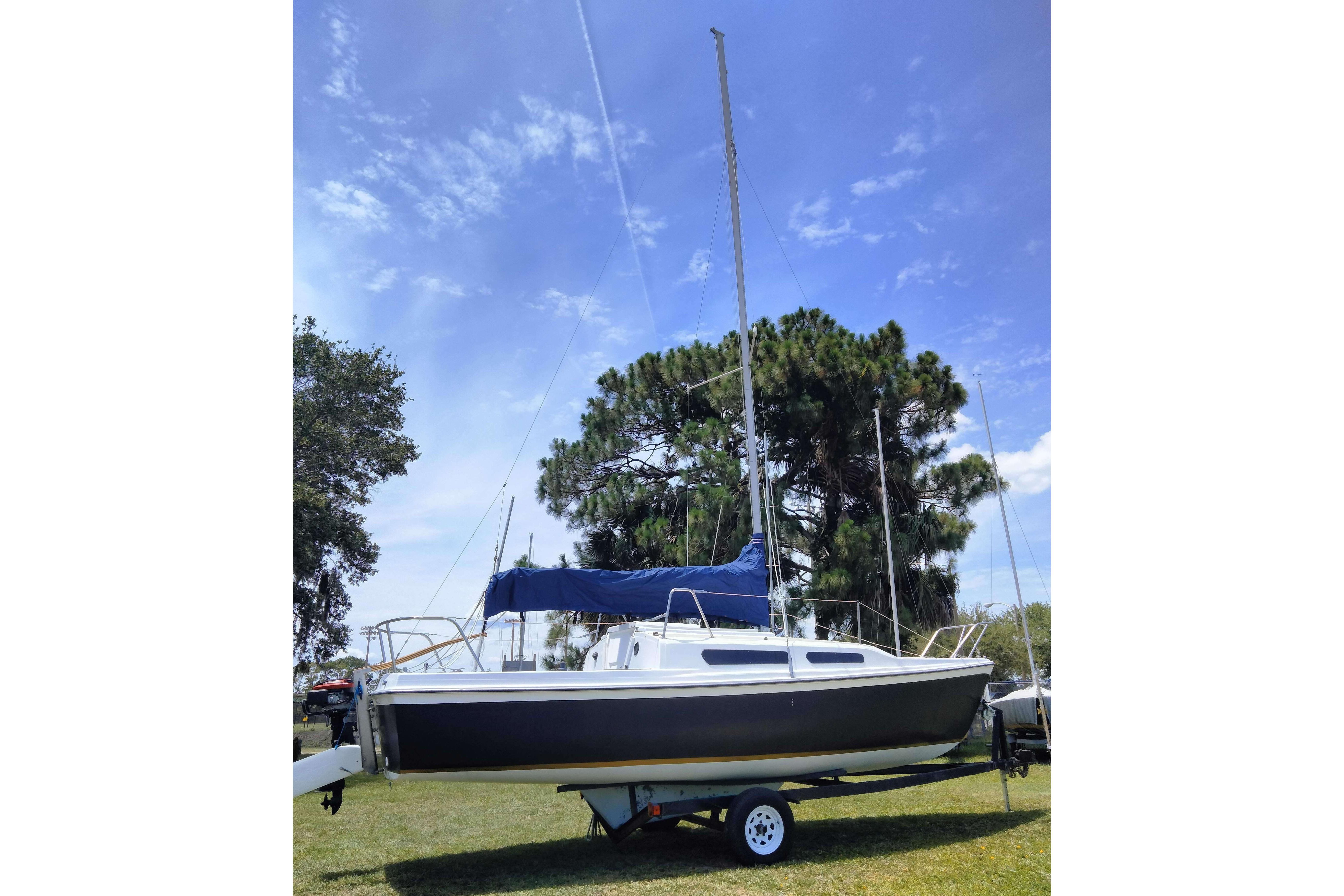 1980 MacGregor 25 sailboat on trailer, set against a clear blue sky and trees.