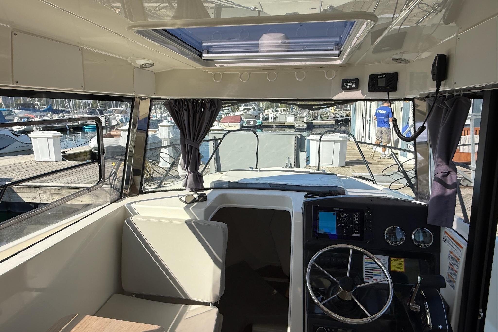 2024 Bayliner Trophy T25 Pilothouse interior with helm, seating, and marina view.