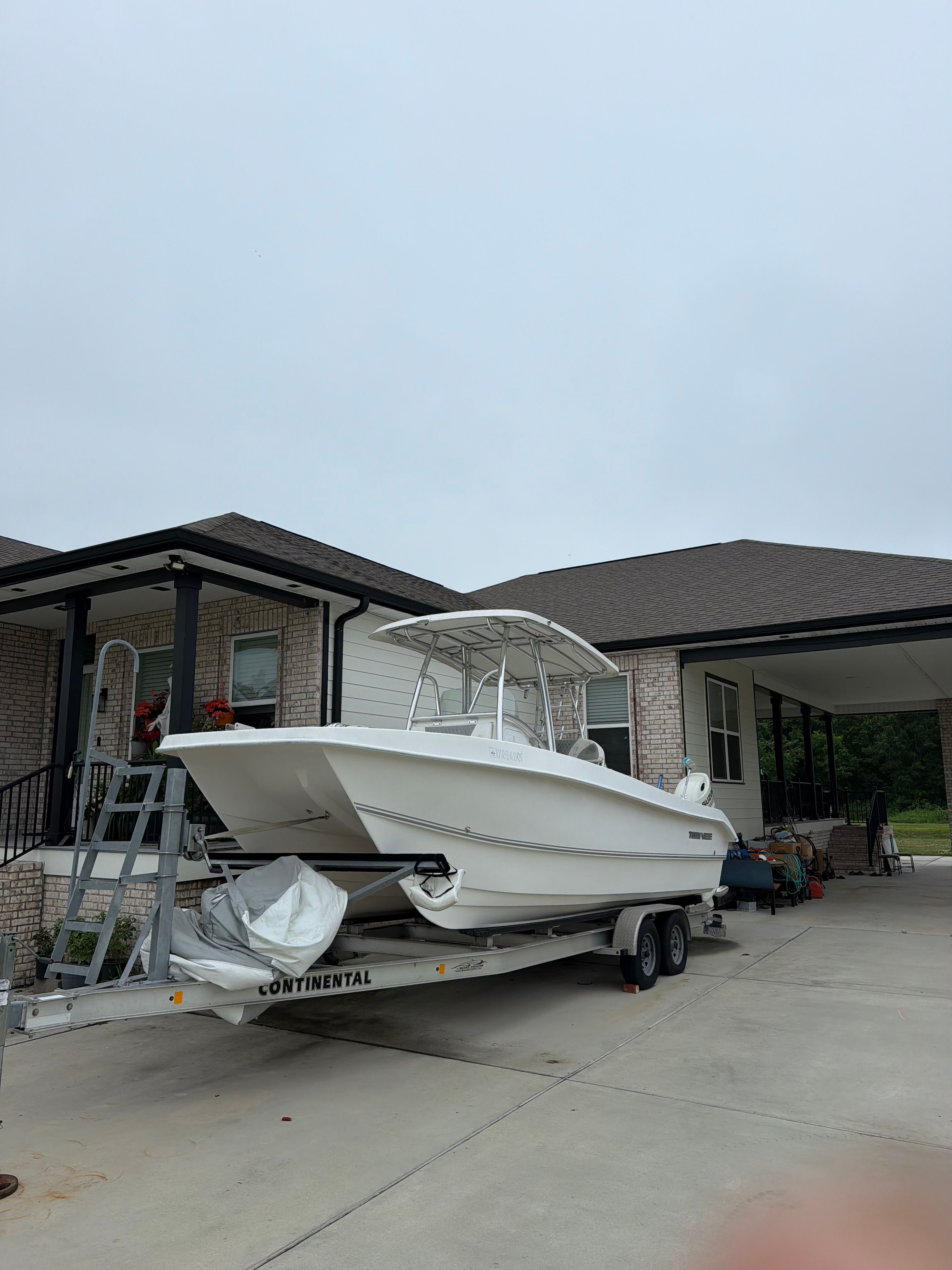 A white boat on a trailer in front of a house.