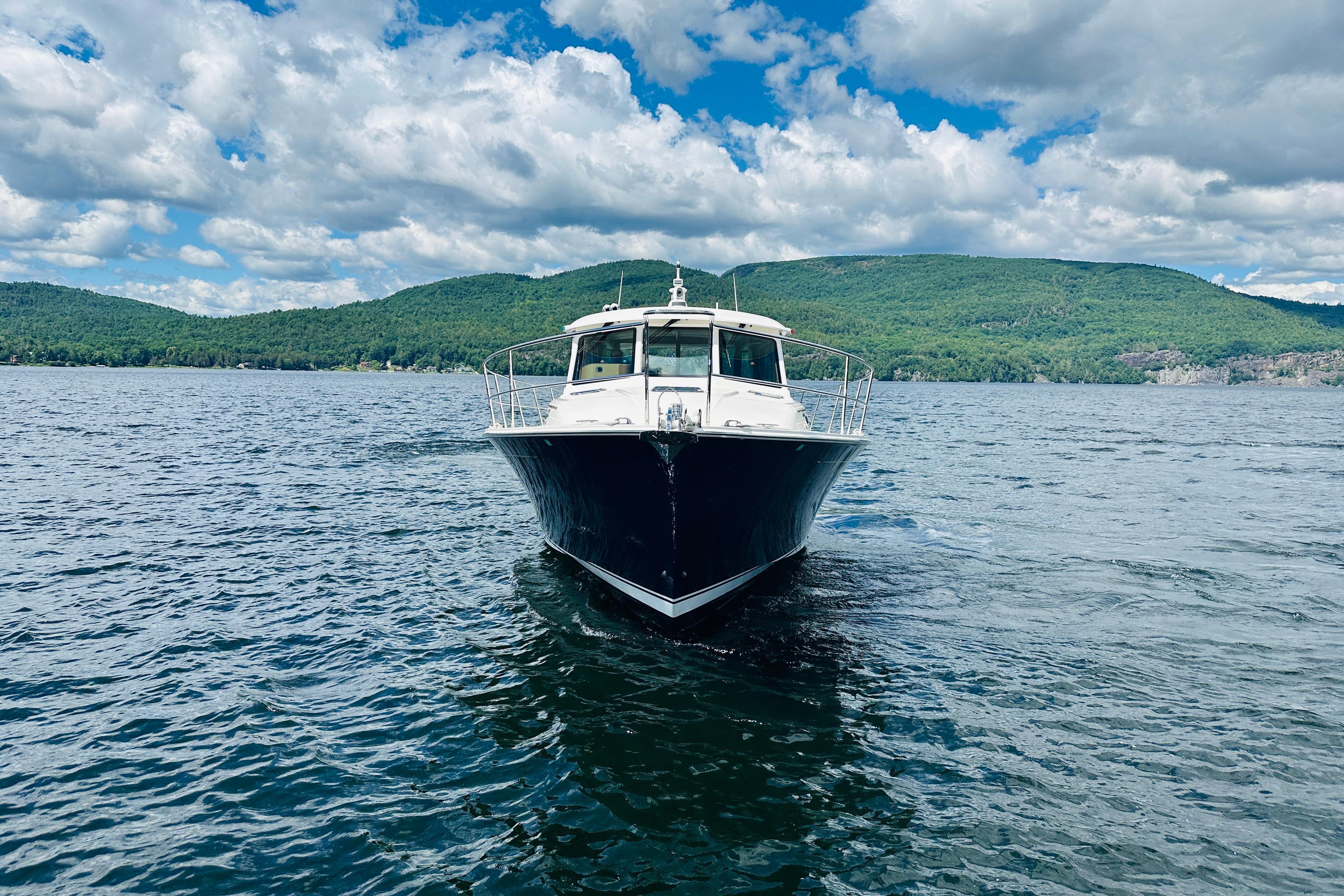2025 Sabre 48 Salon Express yacht cruising on a scenic lake with lush green hills.