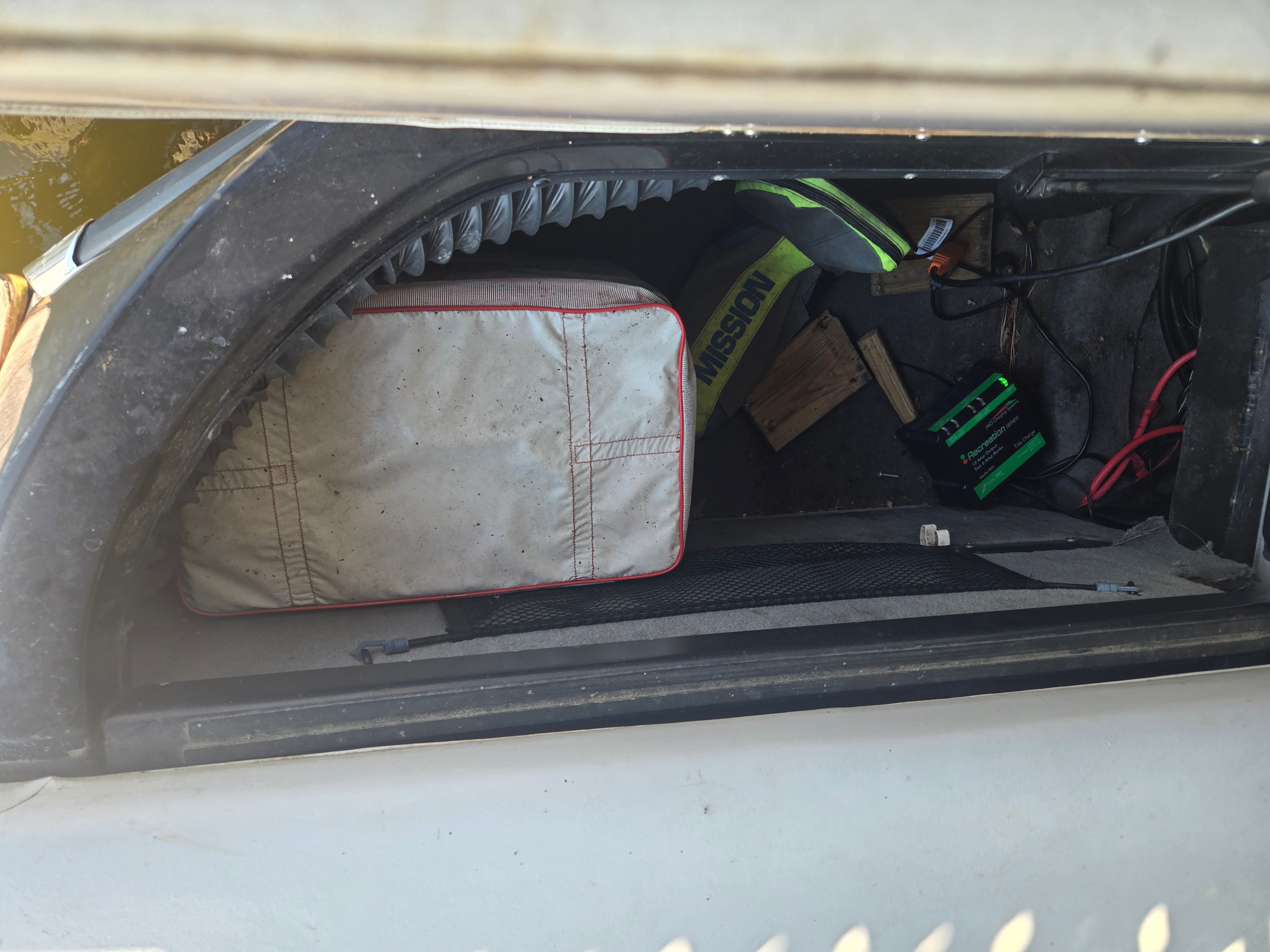 A storage compartment in the boat with a bag and some cables.