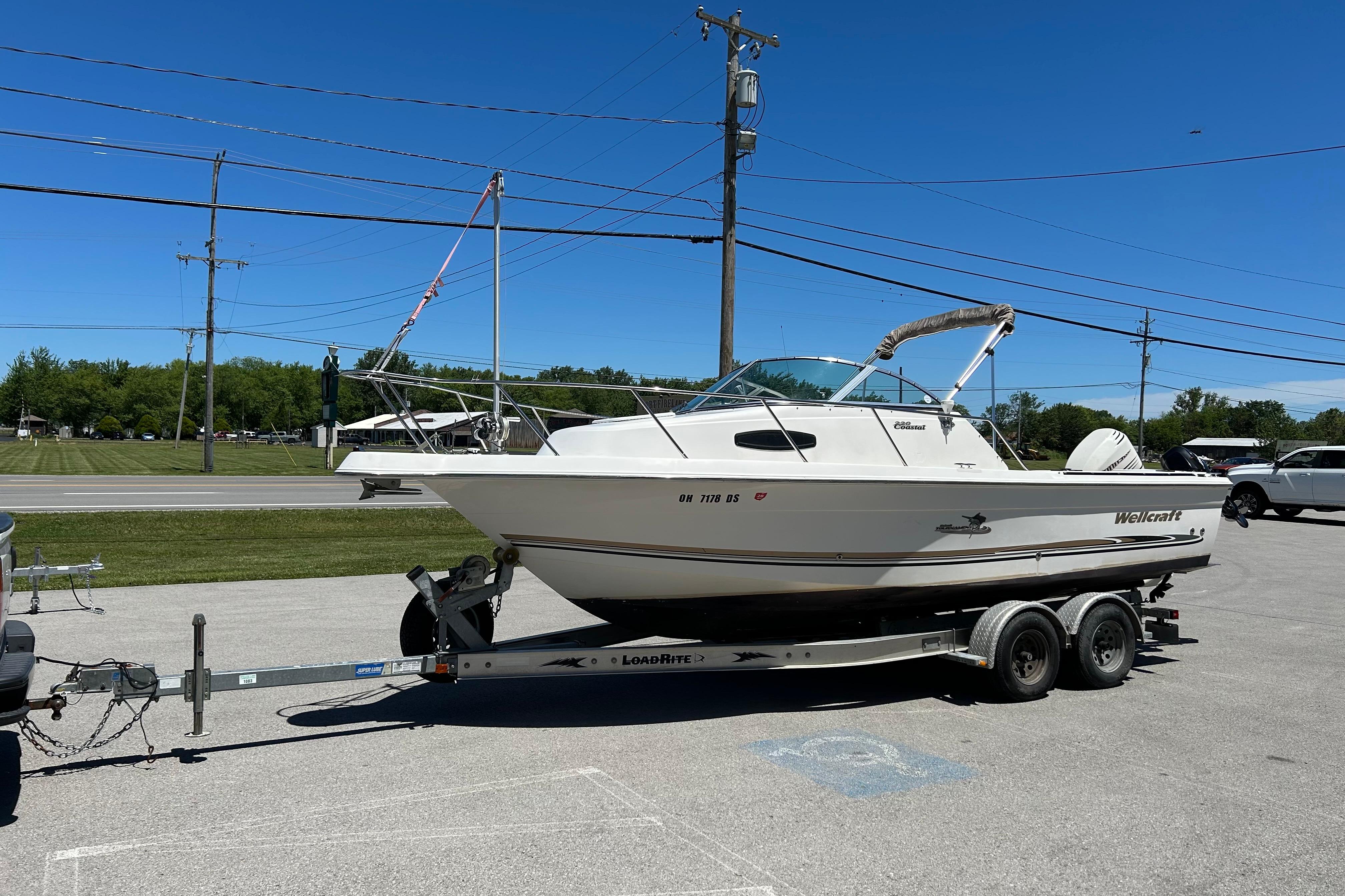 2003 Wellcraft 220 Coastal boat on trailer, parked outdoors under clear blue sky.