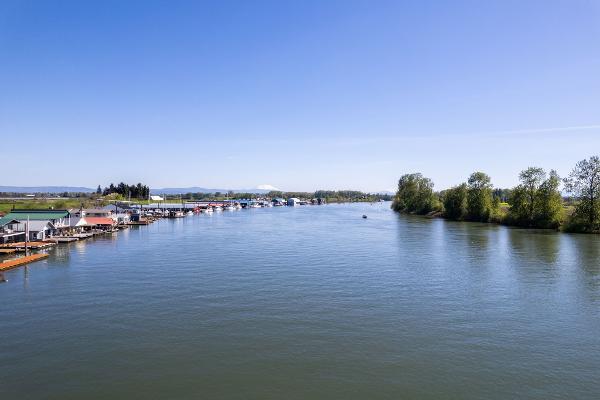 Wide river view with boathouses and trees under clear blue sky, Larson Boathouse, 1985.