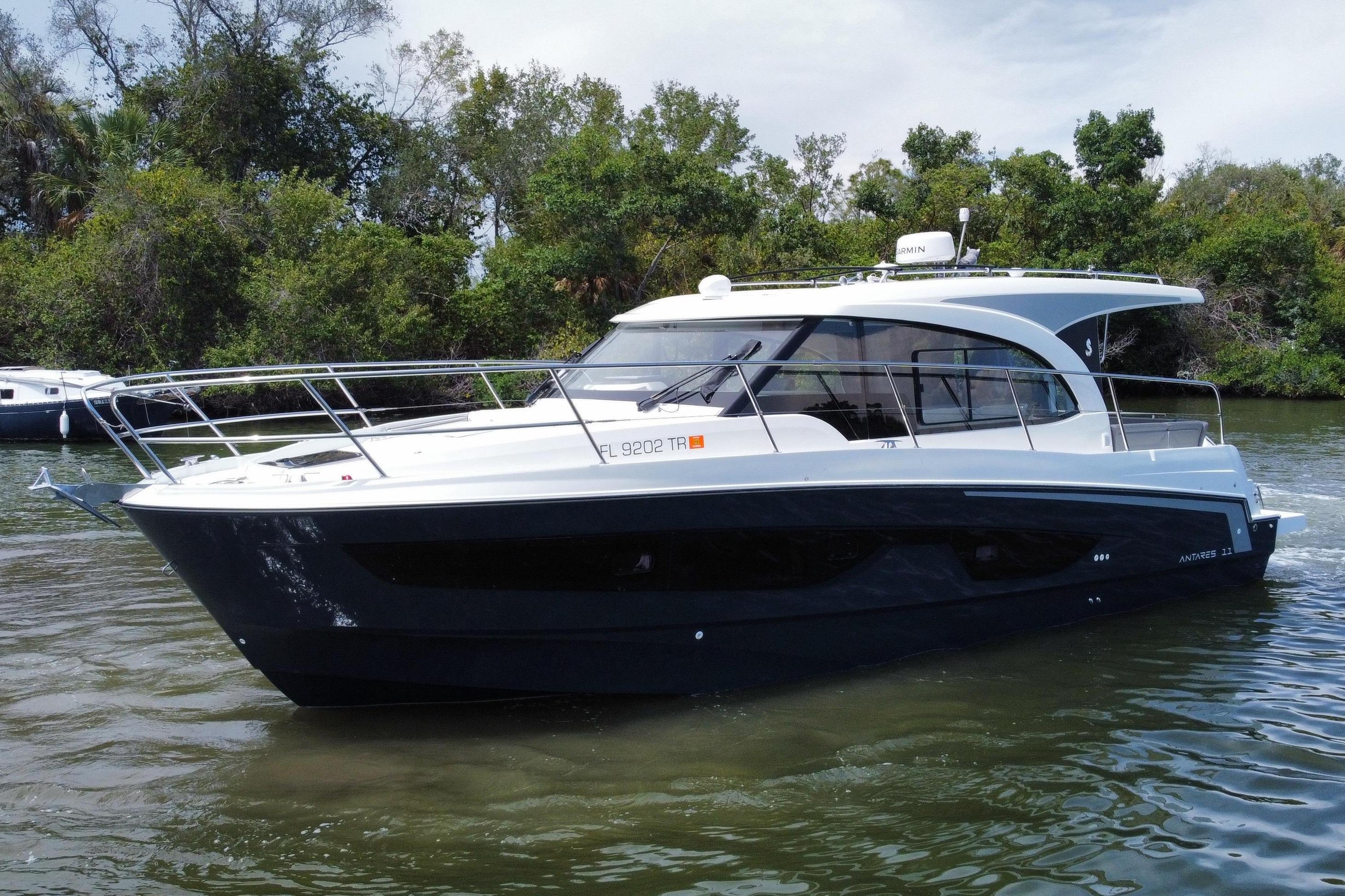 A 2024 Beneteau Antares 11 cruising on calm water, surrounded by trees.