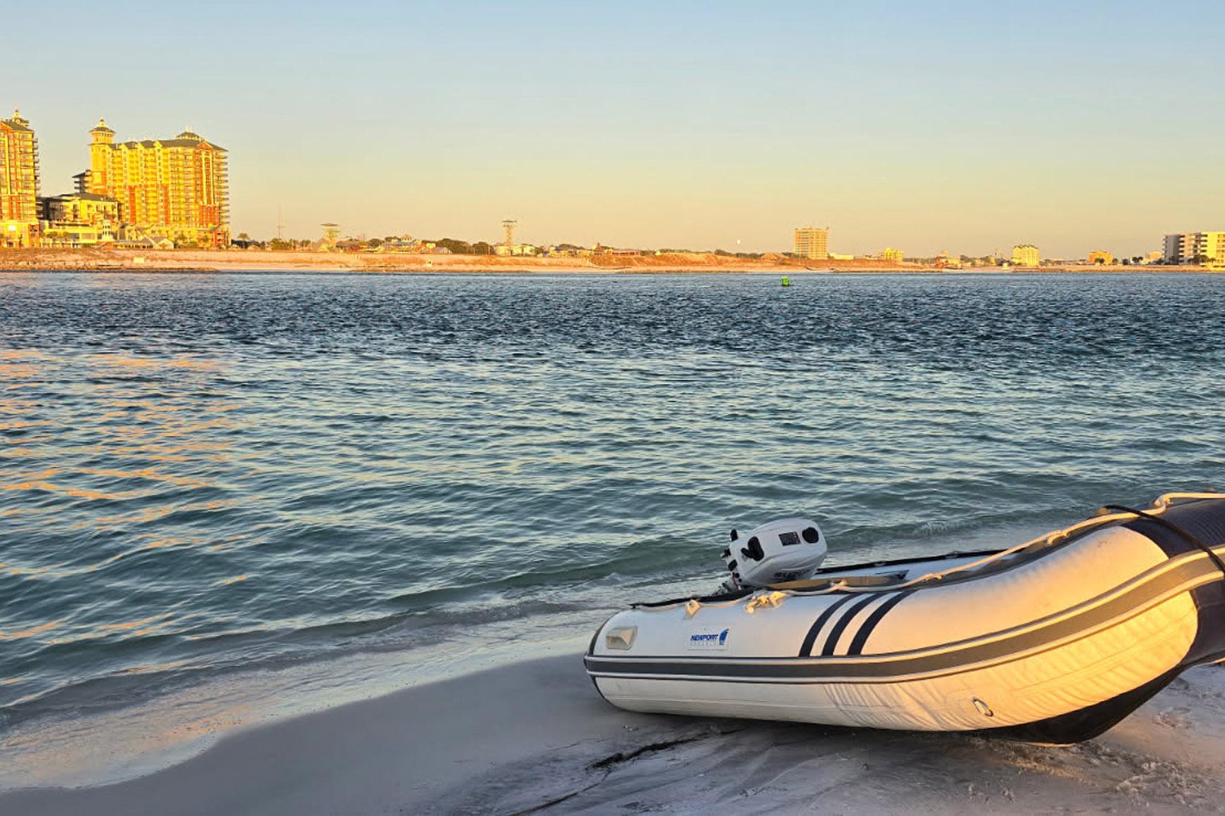 A small inflatable boat on a sandy beach with coastal buildings in the background.