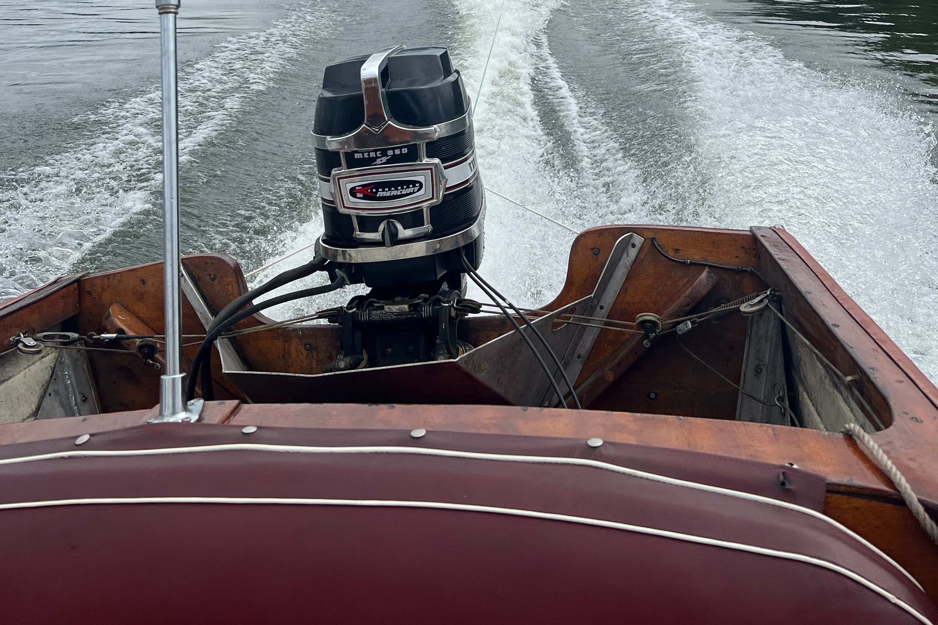 A classic 1957 wooden boat with an outboard motor cruising on a lake.