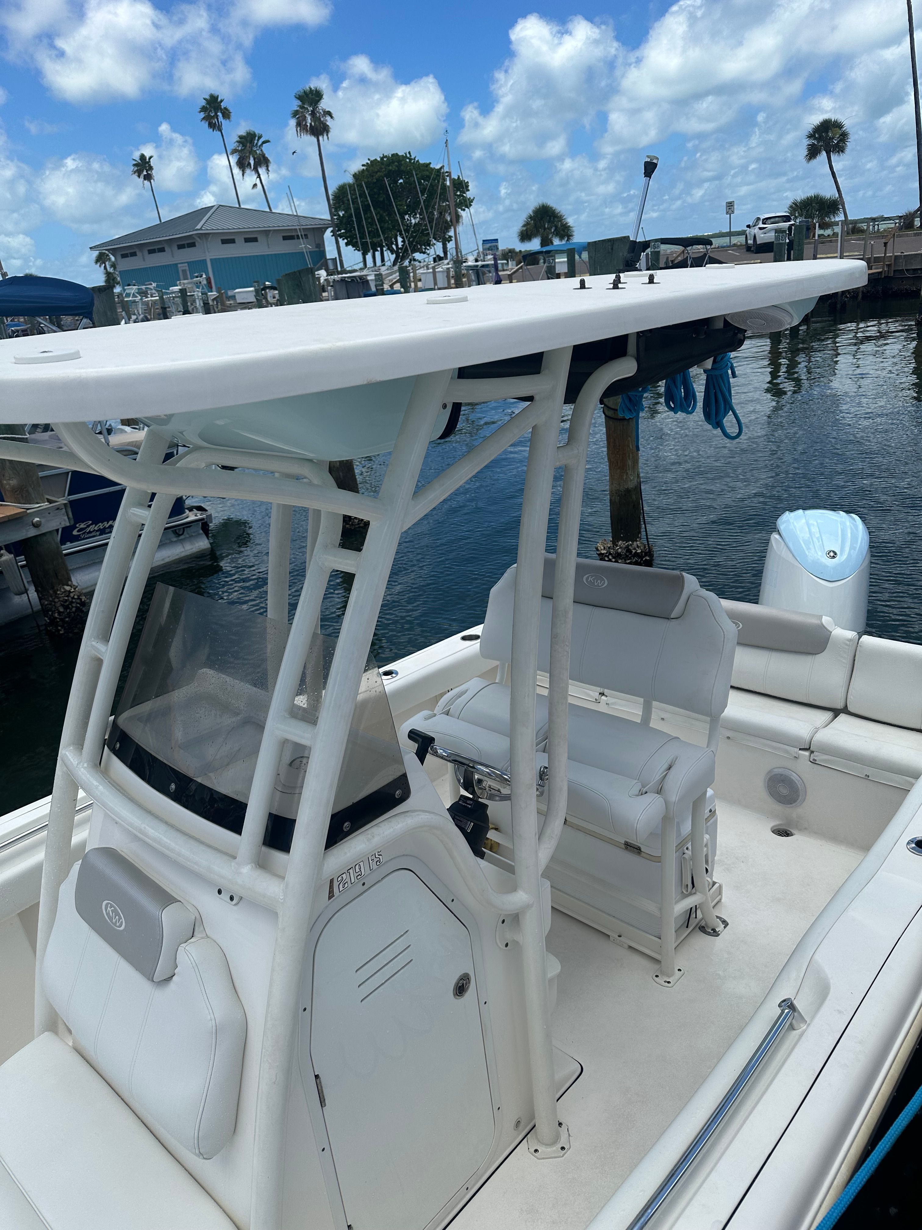 A modern boat with a white canopy and seating area, docked at a marina.