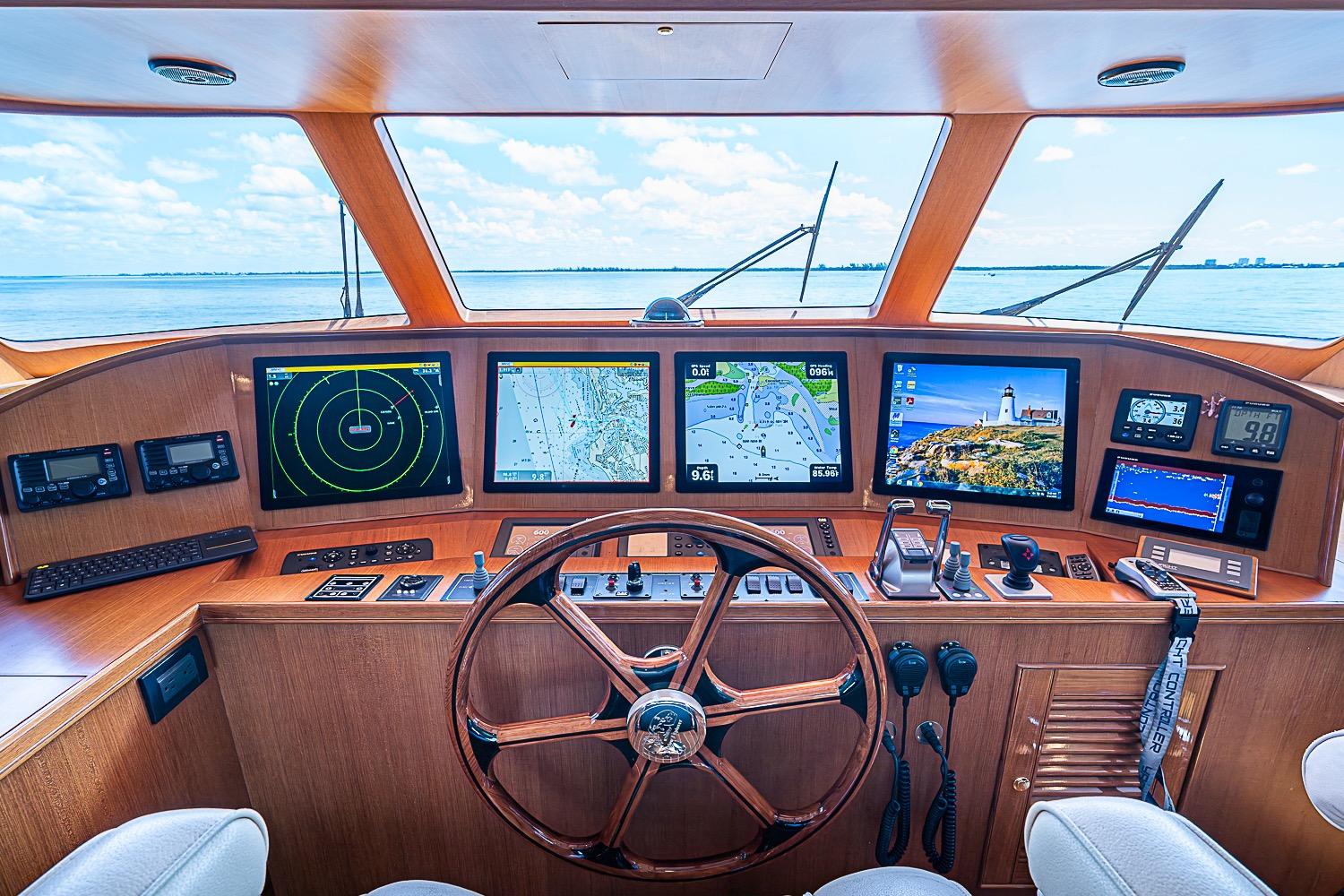 Cockpit of 2014 Marlow 80 Explorer yacht with navigation screens and wooden steering wheel.
